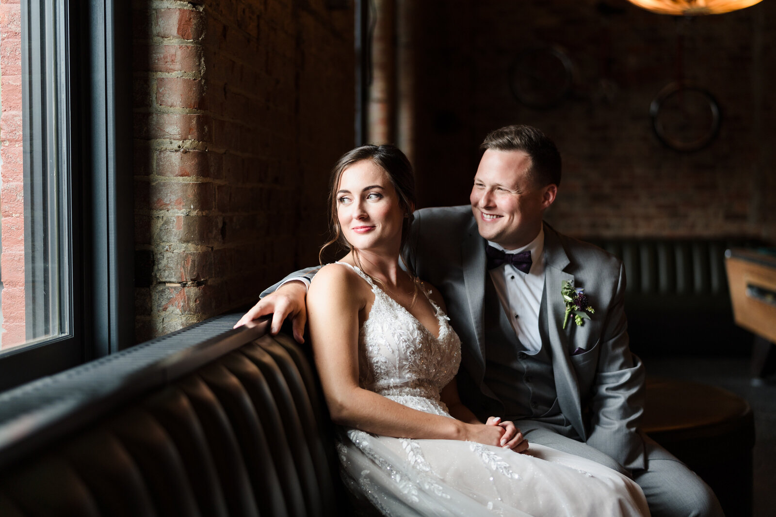 Bride and groom sit on a leather bench and look out the window