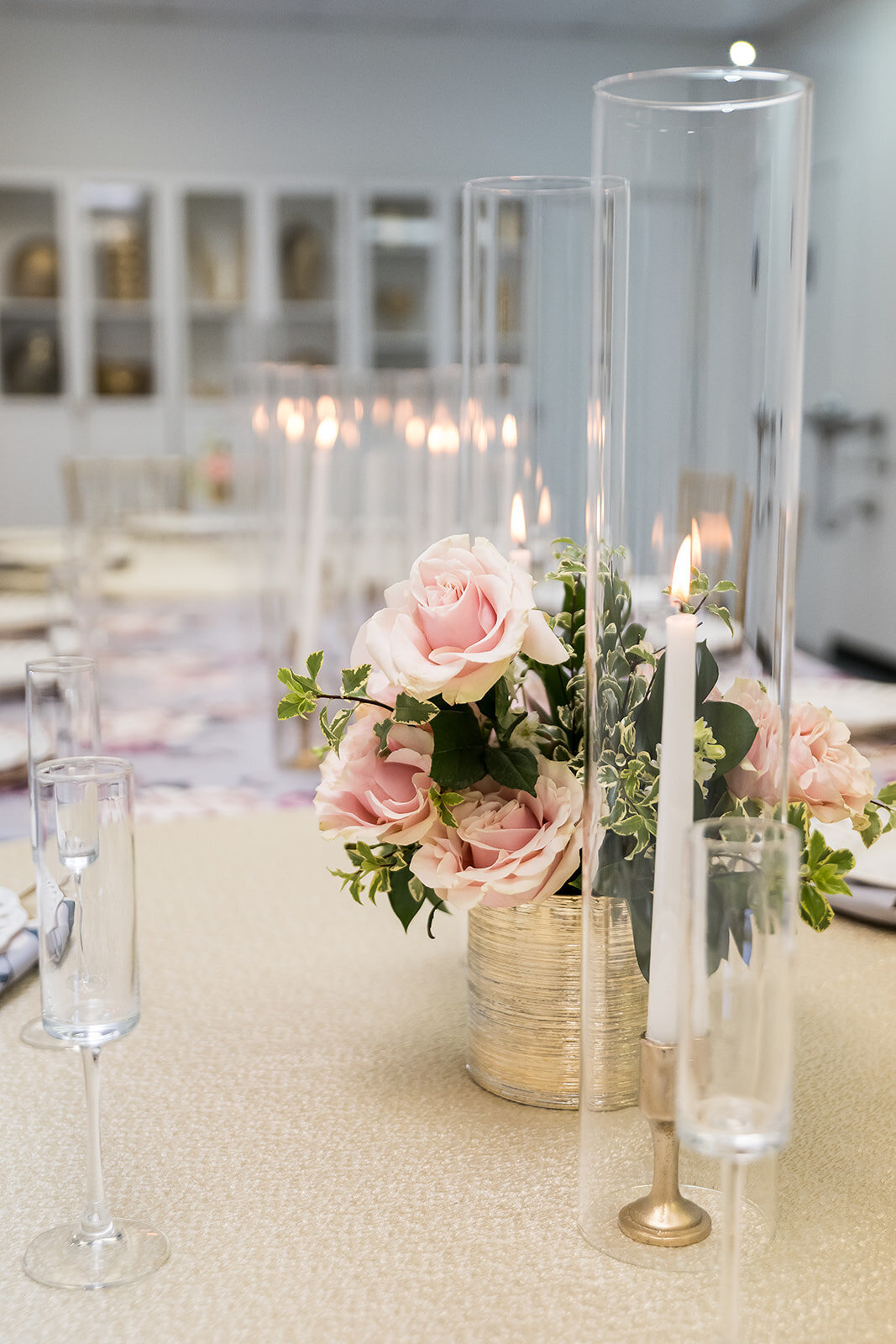 Close-up of blush rose centerpiece with taper candles in glass holders on a textured cream linen table at The Parlor at Wells—perfect for showers, dinners, and styled events.