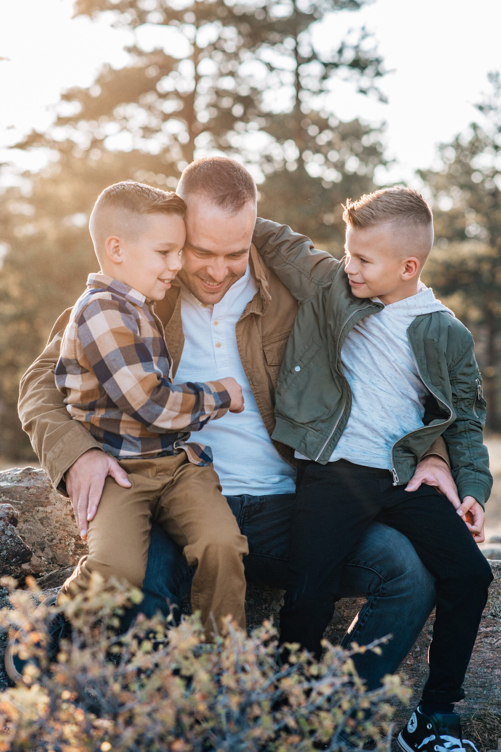 a dad sits on a log with his two sons as they snuggle and talk captured by denver family photographer