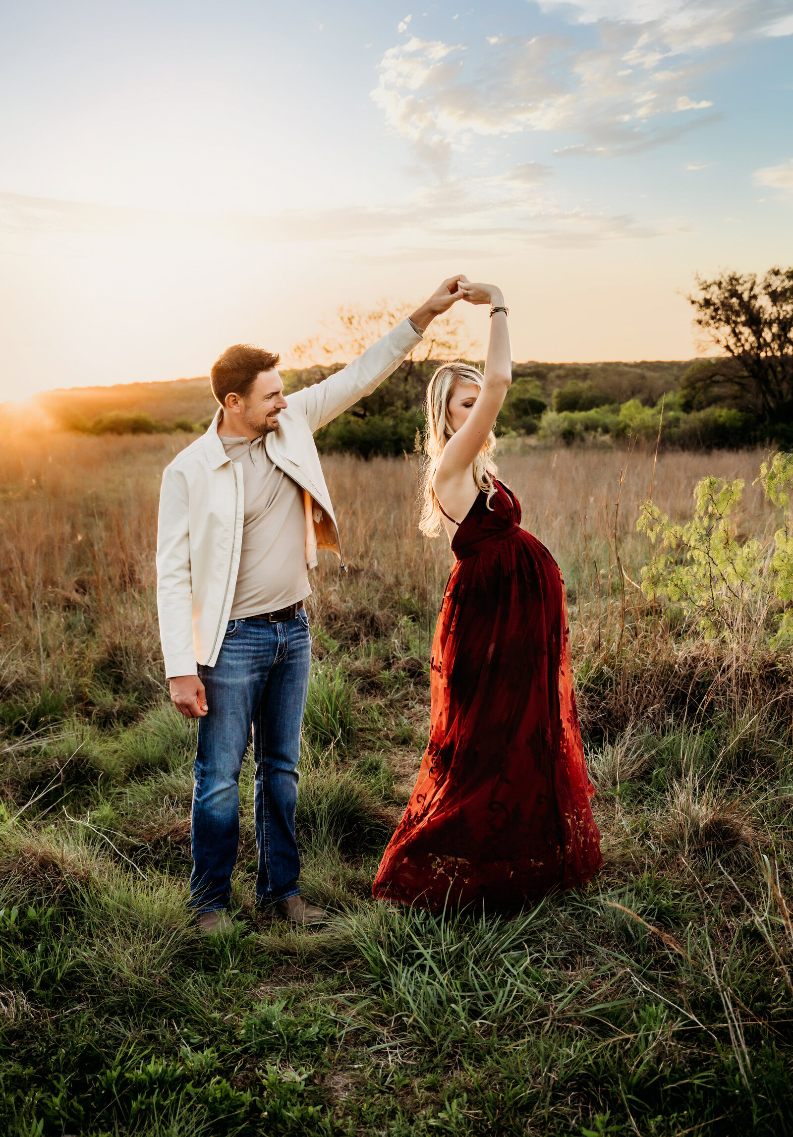 Maternity Photographer, a man spins his wife to dance, she is pregnant and wears a dress in the field