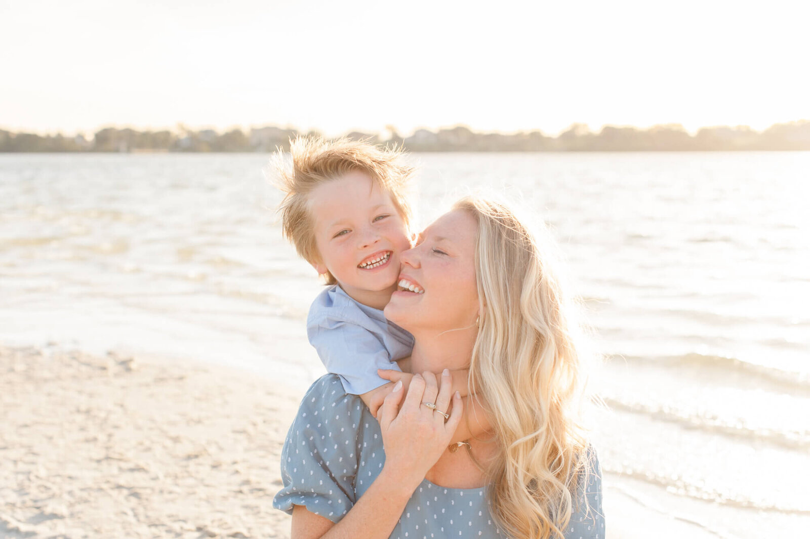 Son grasping mom from behind and laughing with a beautiful golden glow behind her