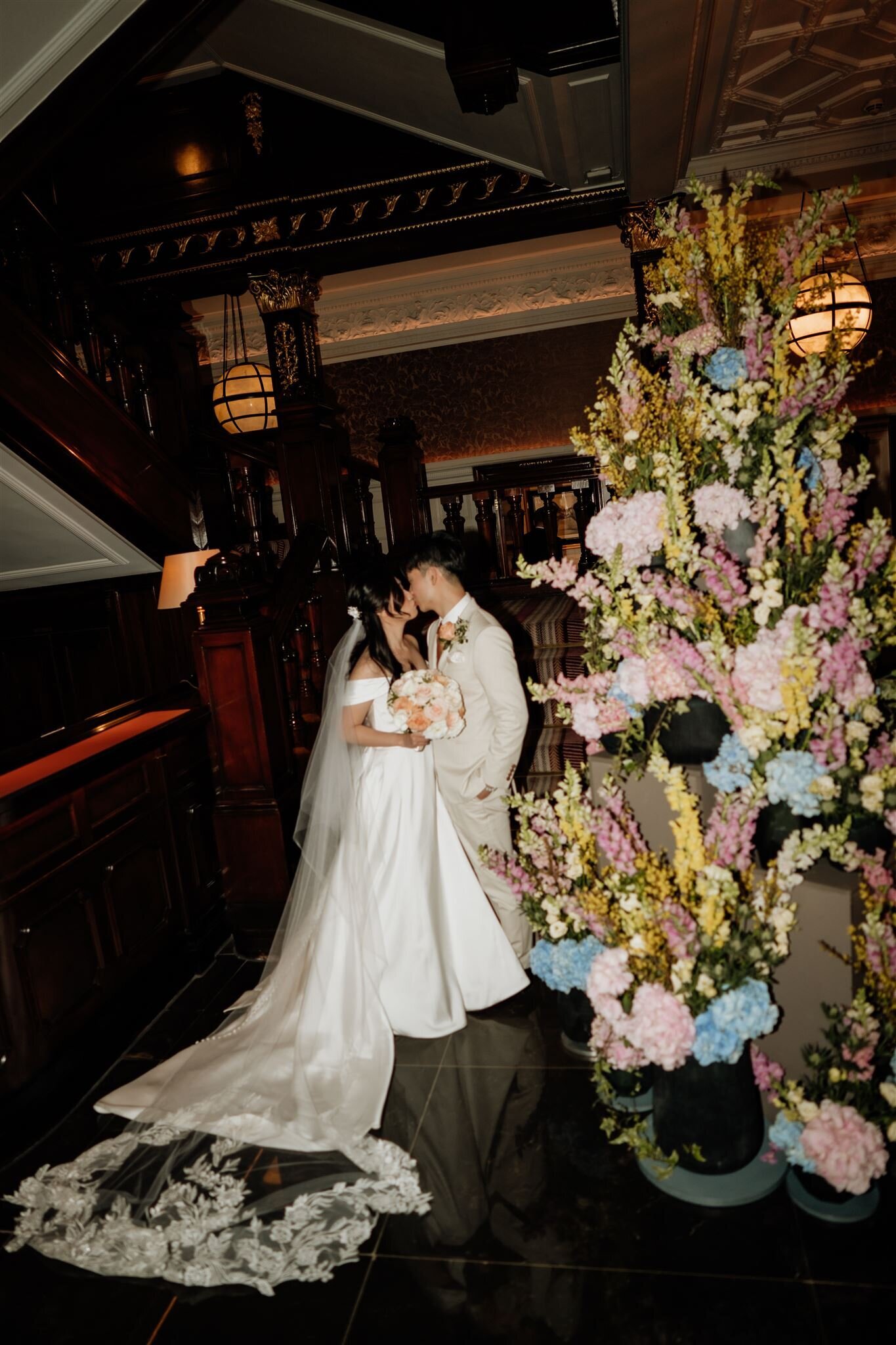 bride and groom kissing next to flowers at the connaught hotel in london