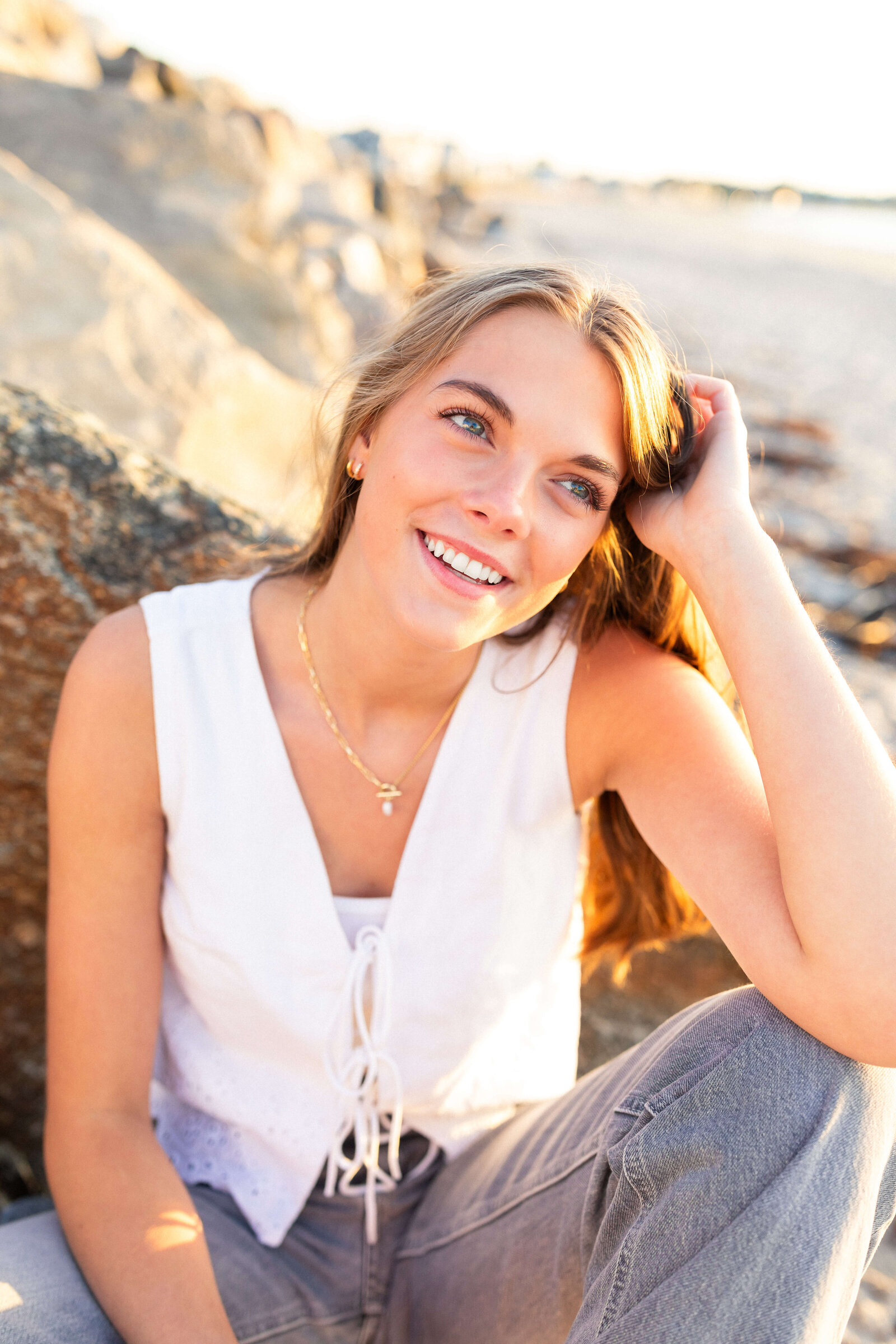 brunette high schooler posing on a beach wearing a white shirt