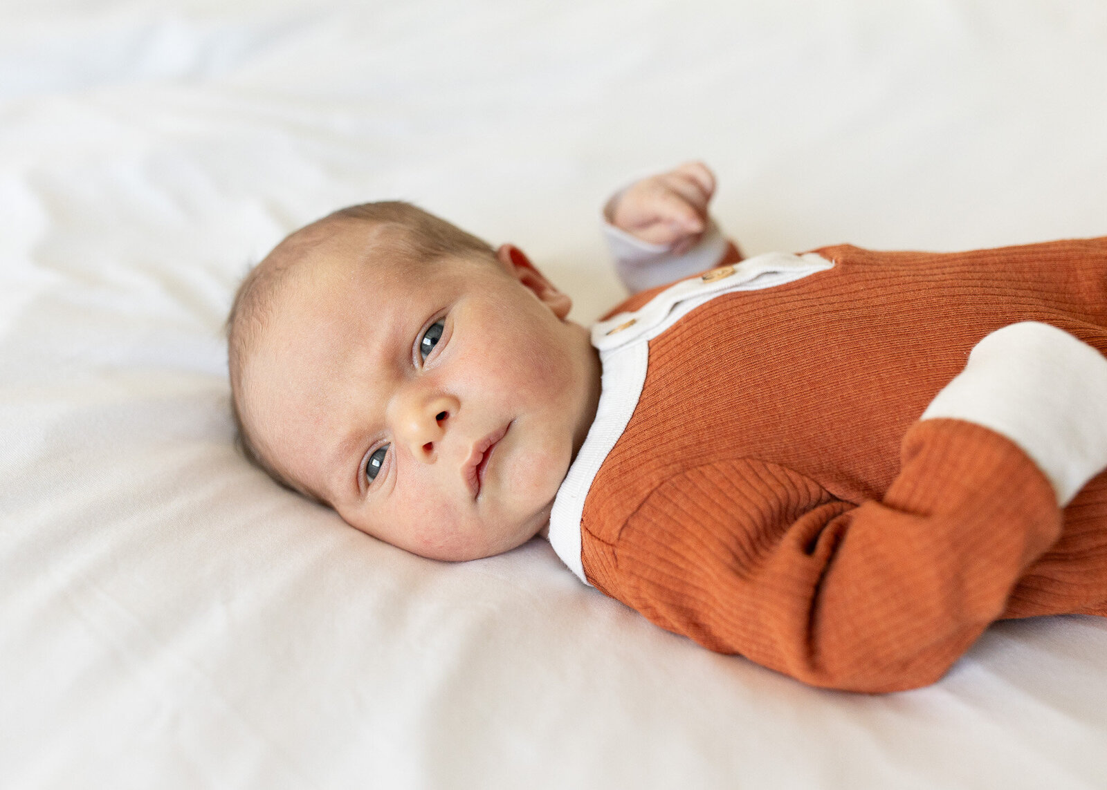 Infant in mustard colored jumper laying on bed.