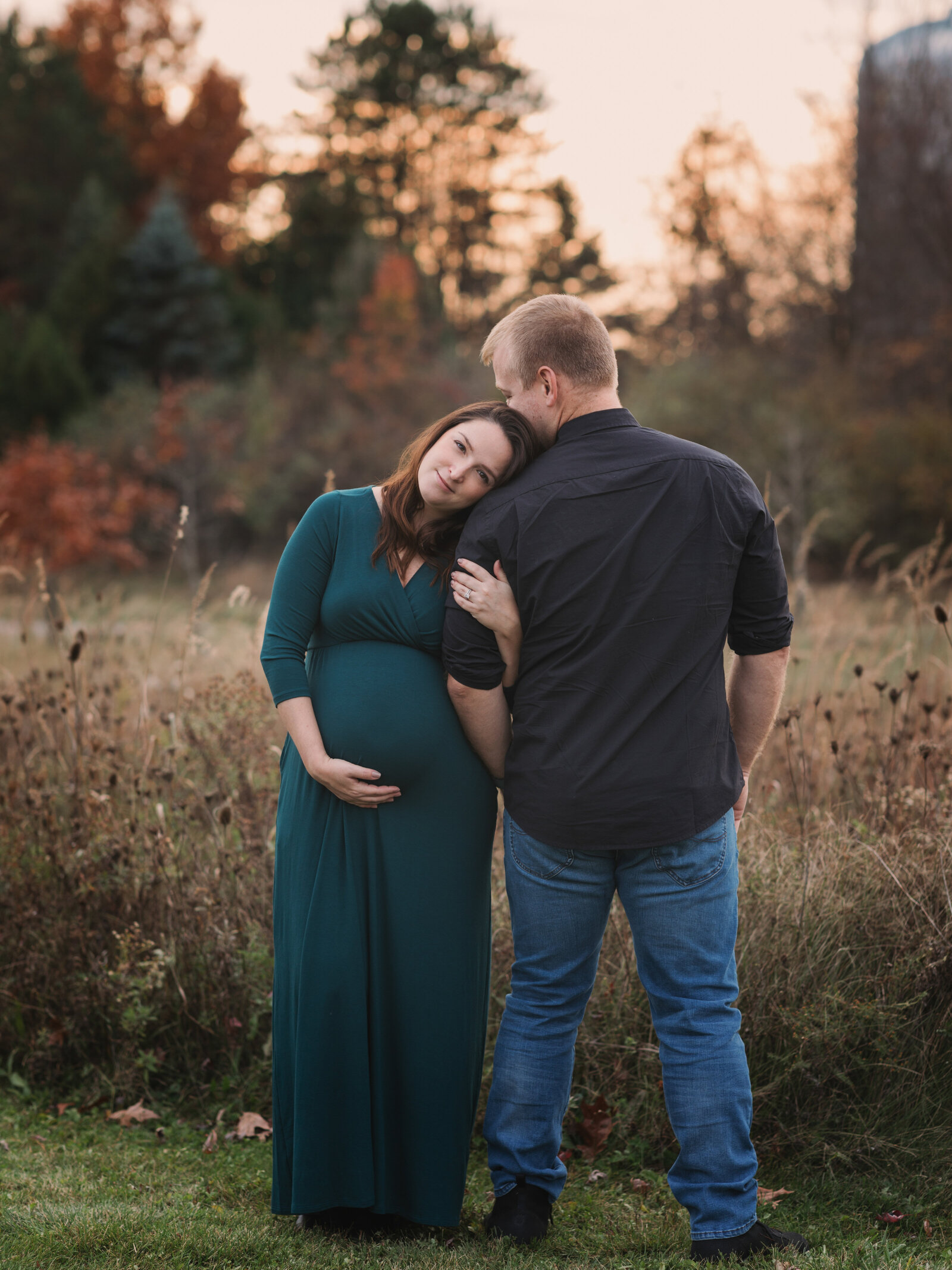 husband and pregant wife in green maternity gown holding baby bump for maternity portraits