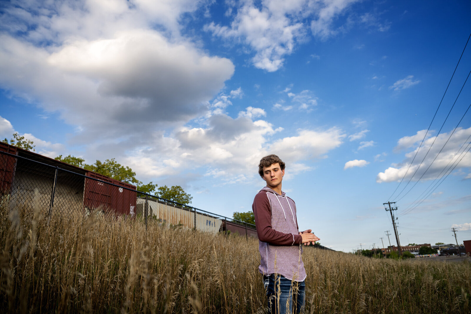 Princeton Minnesota high school senior boy in long grasses with train and dramatic blue skies
