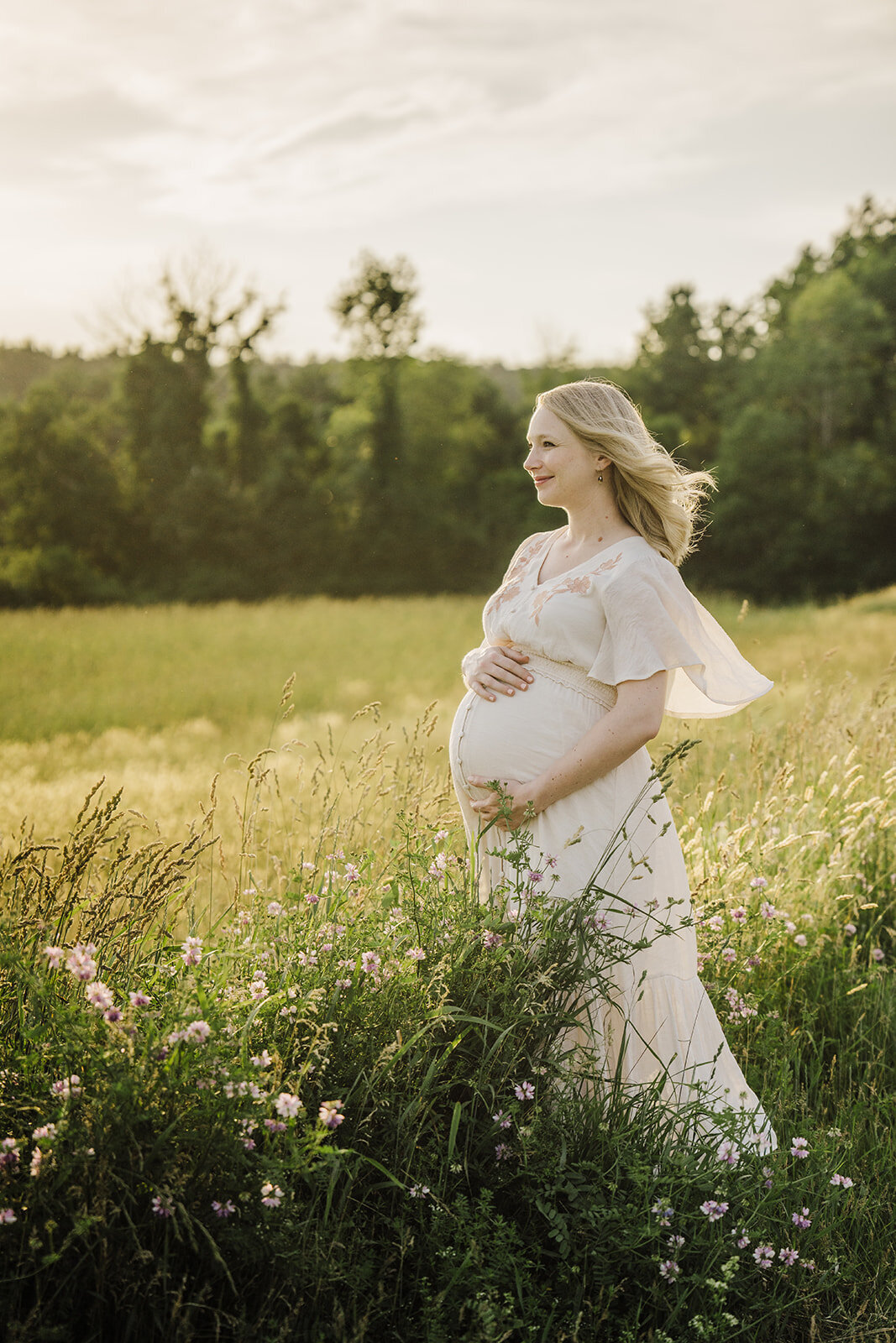 pregnant woman stands in field with wind blowing hair