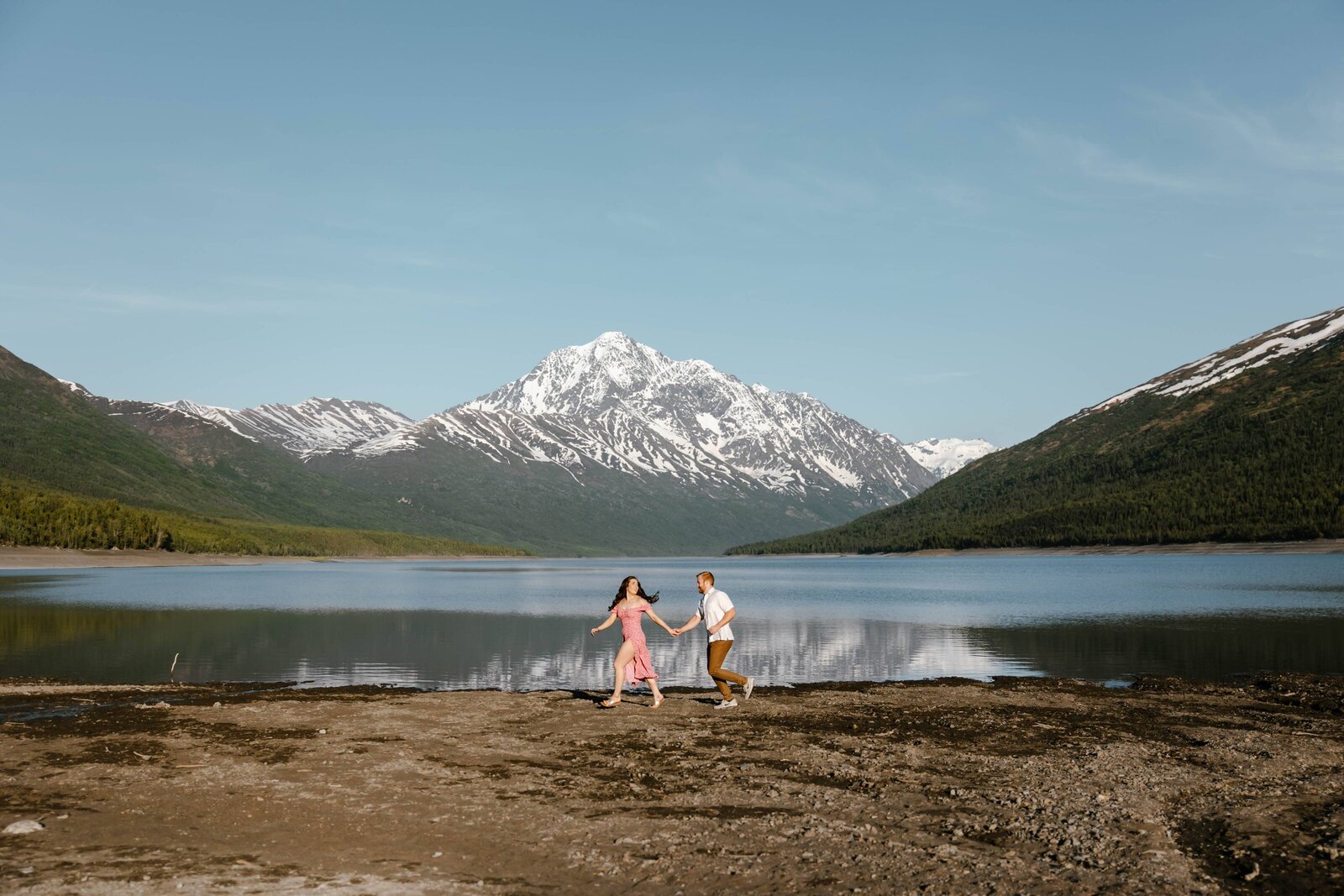A couple running on the beach of Eklutna Lake during an engagement session