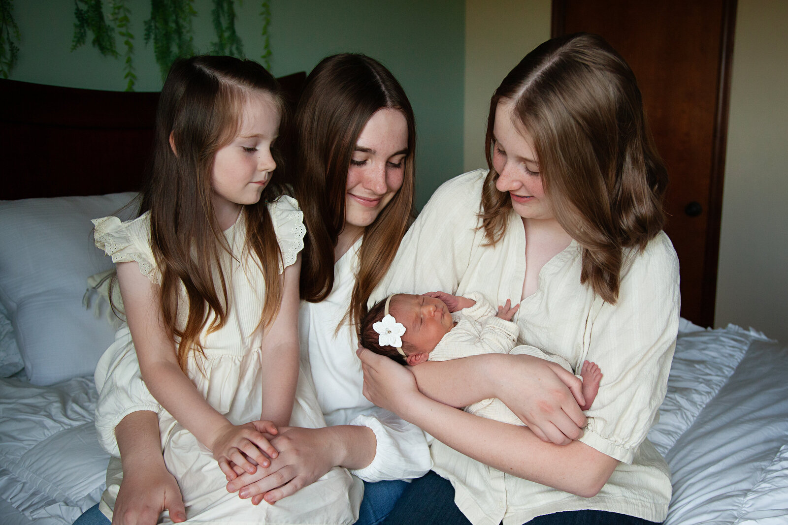 Three older sisters holding their new baby sister in their home.