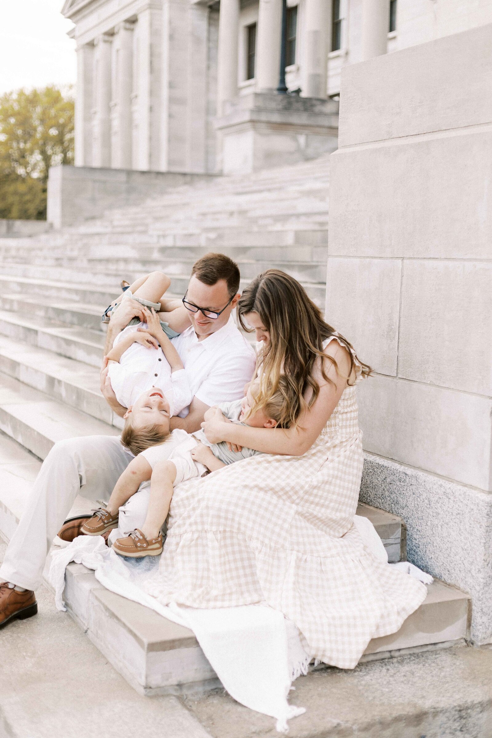 family laughing and playing on steps during maternity photos in peoria illinois 