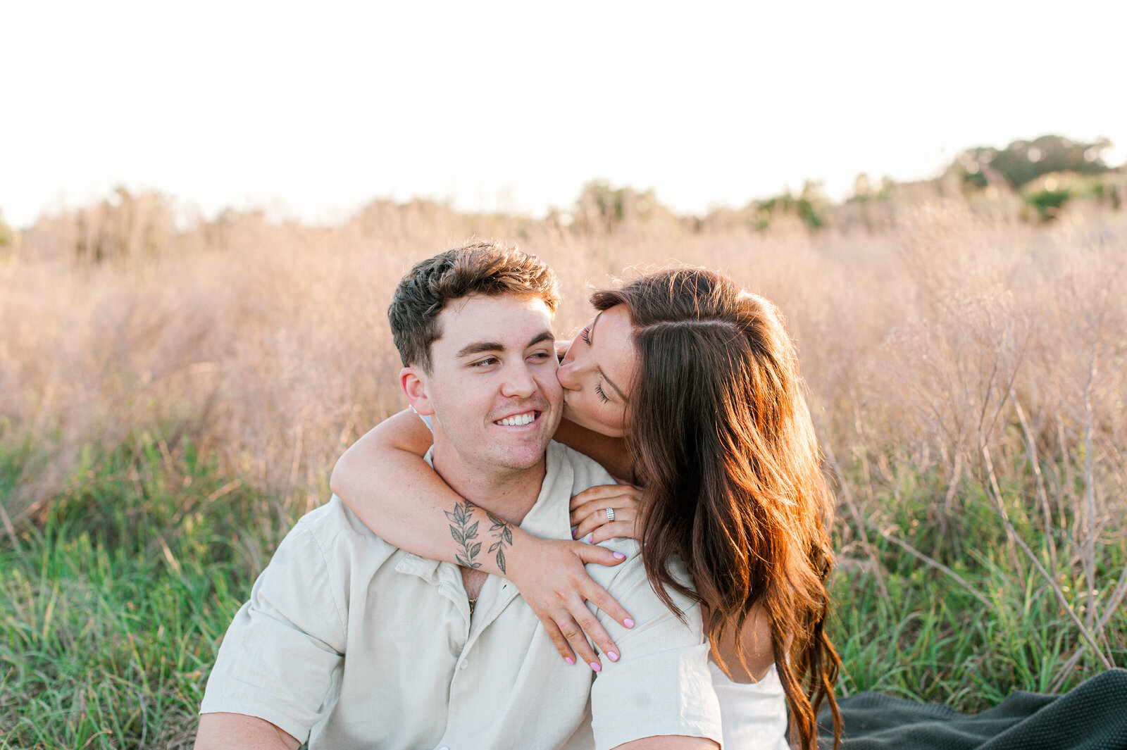 Girlfriend kissing her mans cheek in a tall grass field at sunset in Orlando