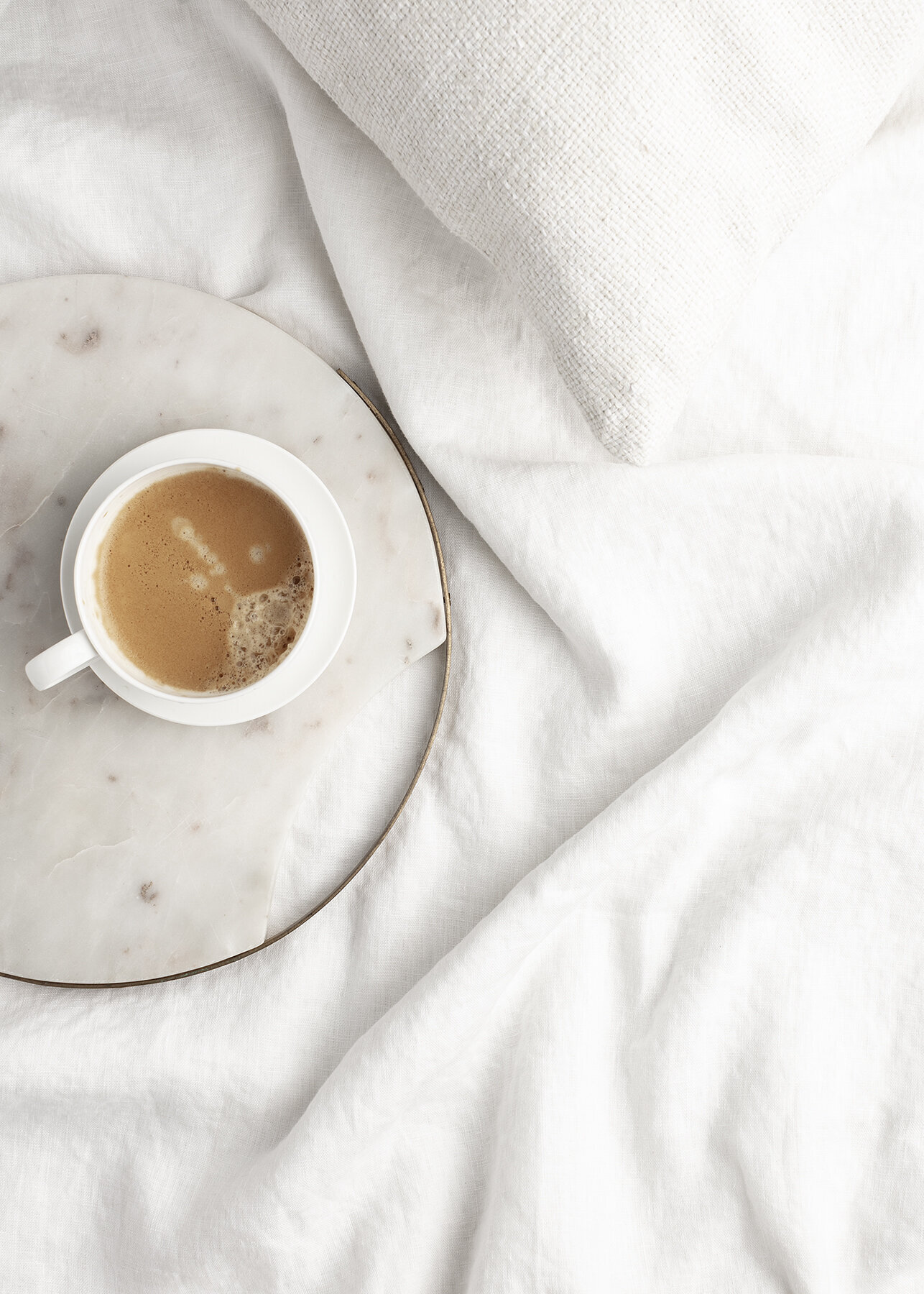 A coffee mug sits on a marble tray on top of a white sheet.