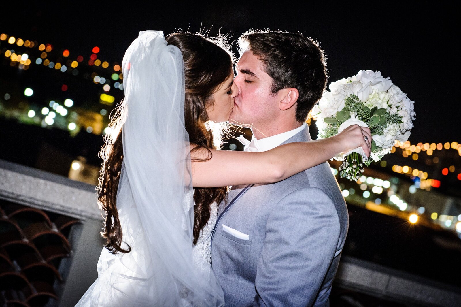 Bride and groom kiss at night on top of Omni Royal Orleans Hotel