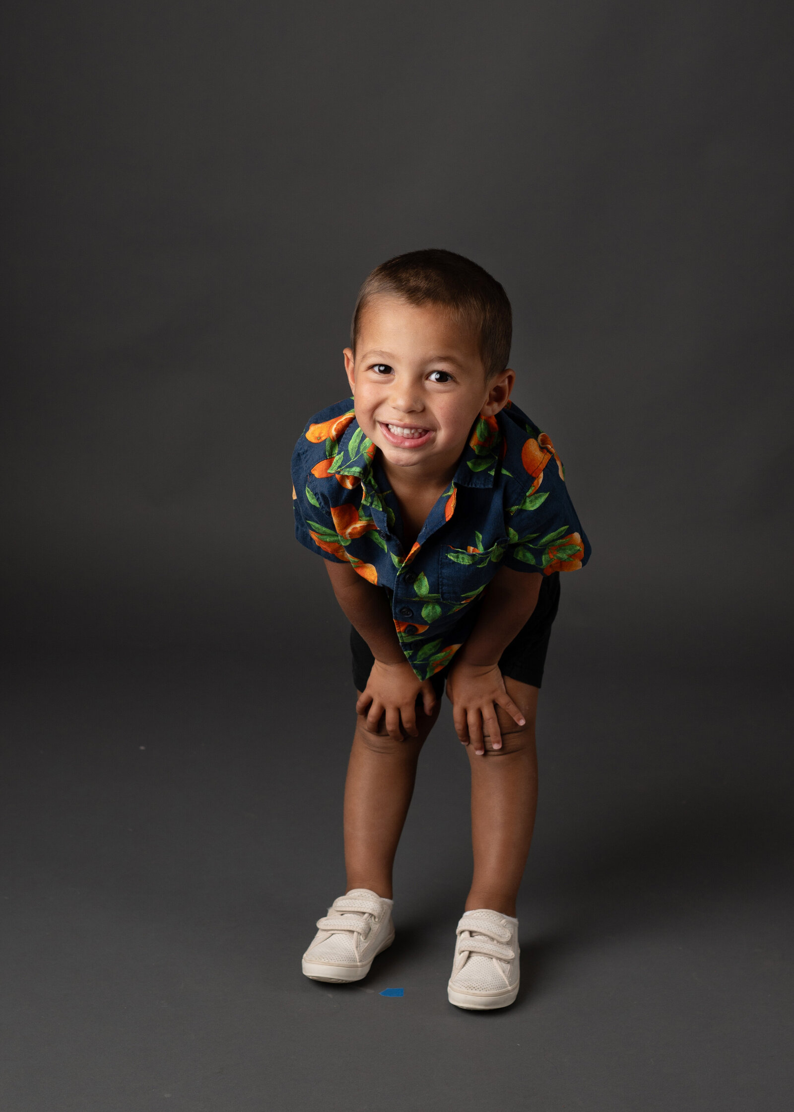 A cute young boy smiling with his hands on his knees.