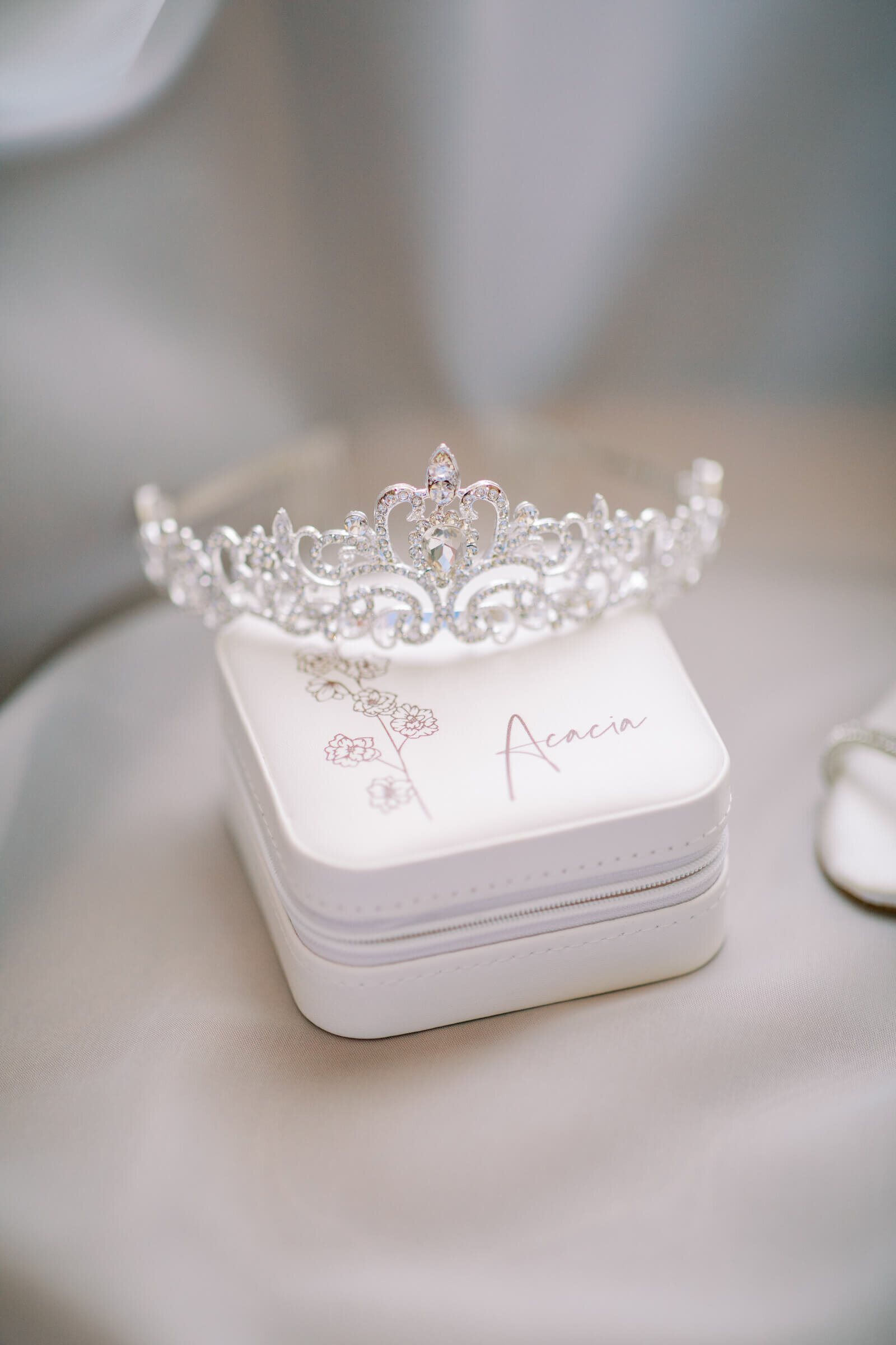 Een fijn afgewerkte tiara ligt bovenop een gepersonaliseerd doosje, symbool voor verfijning en stijl op een bruiloft.