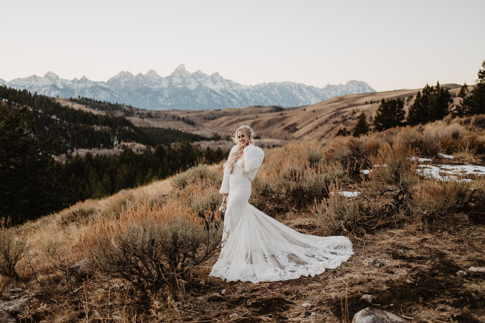 fall wedding with bride in a lave wedding gown posing on a hill  next to the wedding tree with the hills, forest and mountains behind her captured by jackson hole wedding photographer