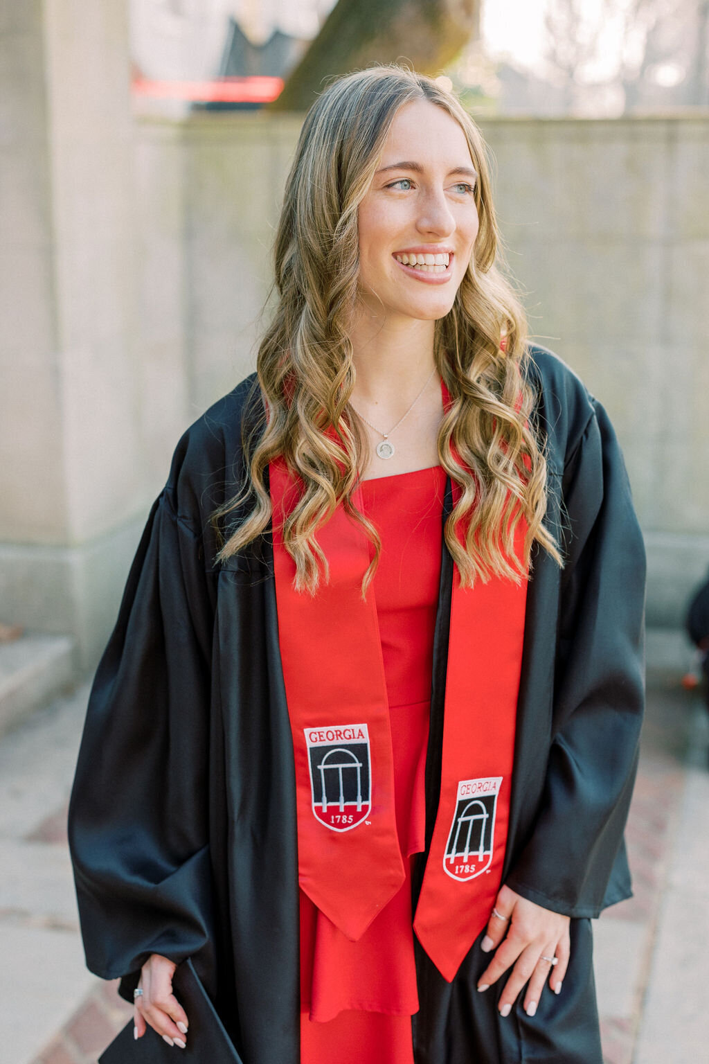 Woman in graduation gown smiles on UGA campus