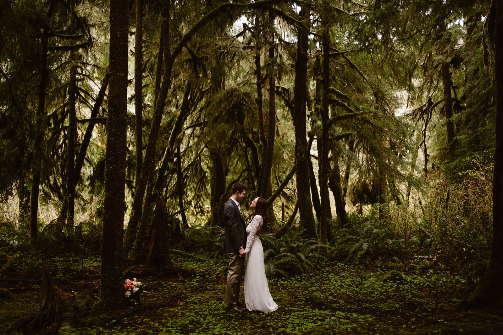 a couple in wedding attire embraces in a grove of mossy trees at their Washington elopement