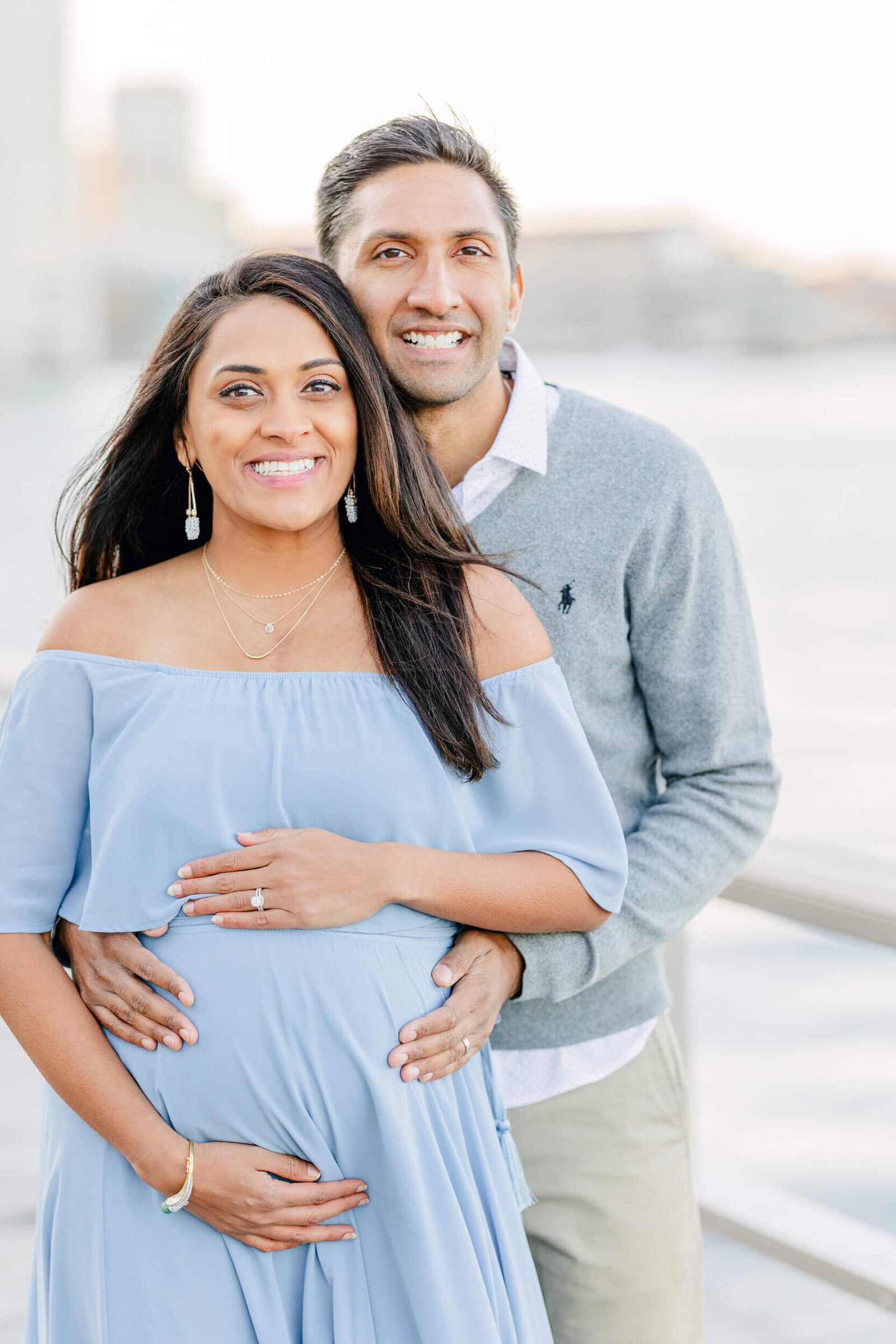 Pregnant woman and her husband smile in front of Boston harbor