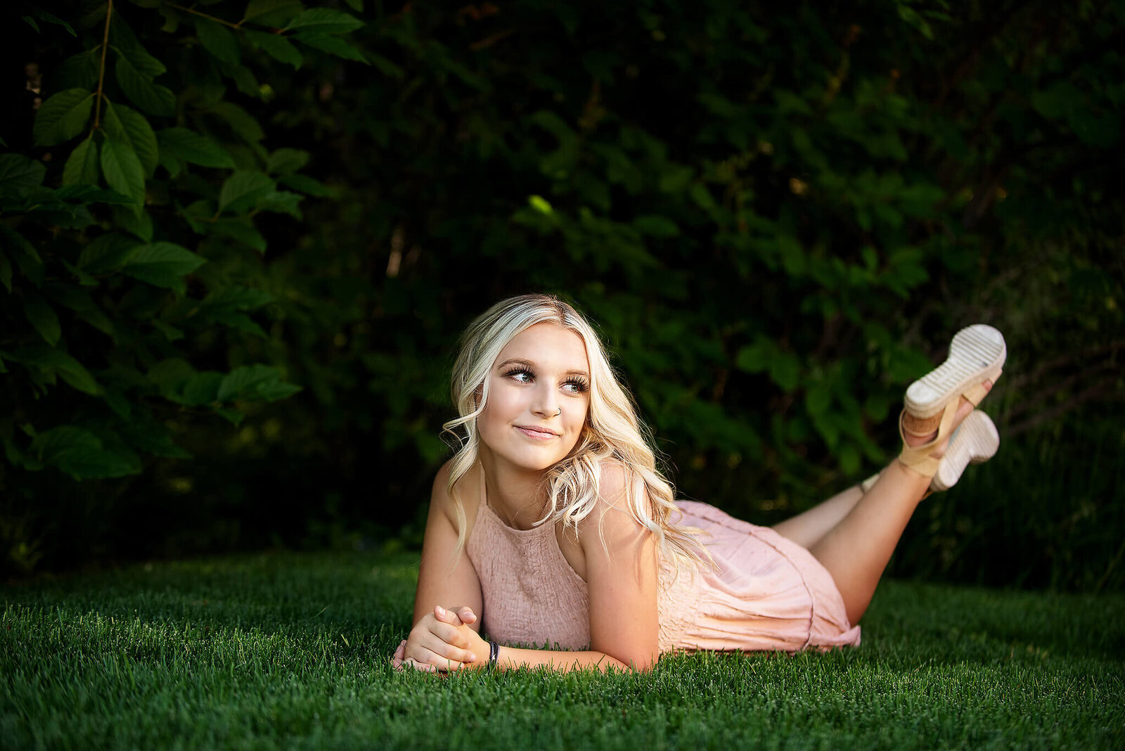Senior girl wearing  a pink dress laying in the grass near Pinedale Wyoming