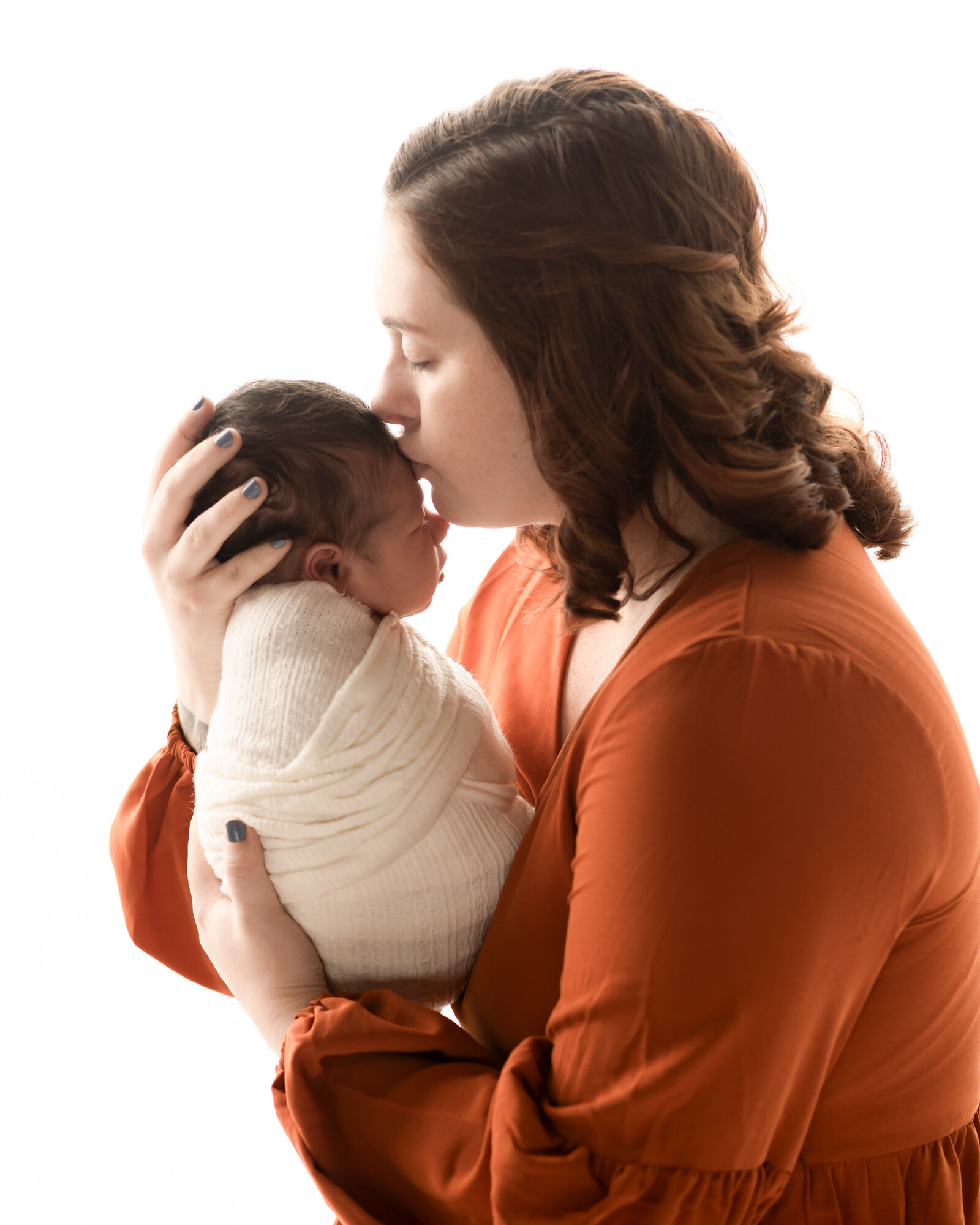 mom kissing newborn baby boy on head for studio portraits