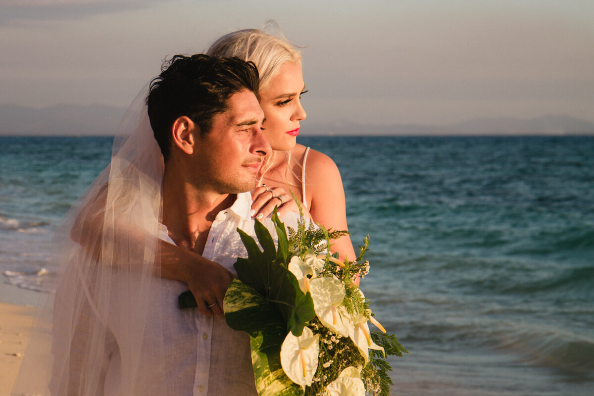 Bride and groom looking out to sea at sunset