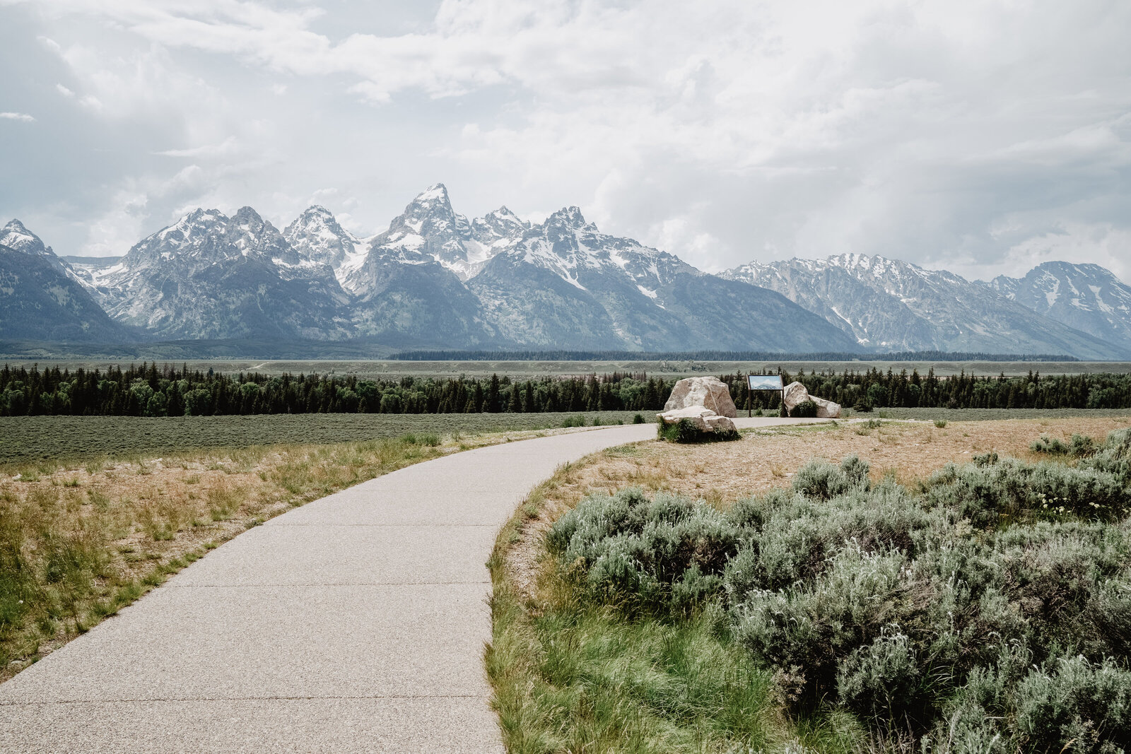 jackson hole wedding location at Glacier View Turnout with a frieldly concrete sidewalk the leads to a boulder with the grand tetons in the distance for the perfect view of the mountains