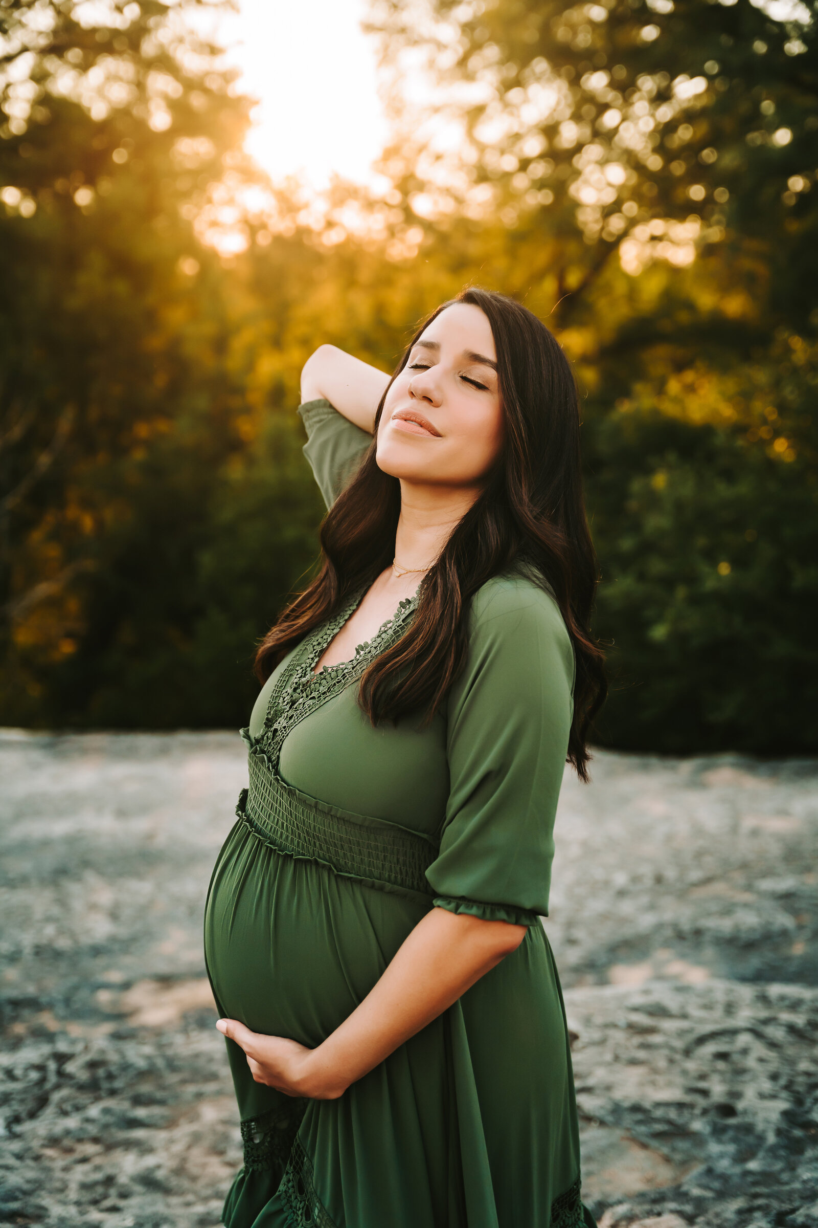 Maternity Photographer, a woman holds her belly, she wears a dress in the forest