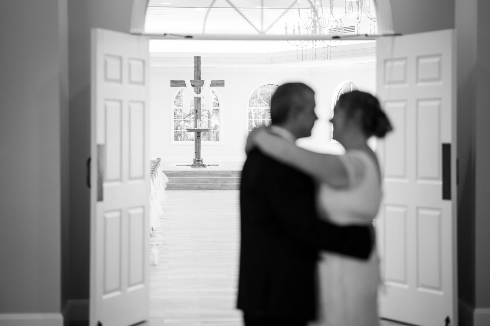 A bride and groom share their first dance as the camera focuses on a large cross in the background
