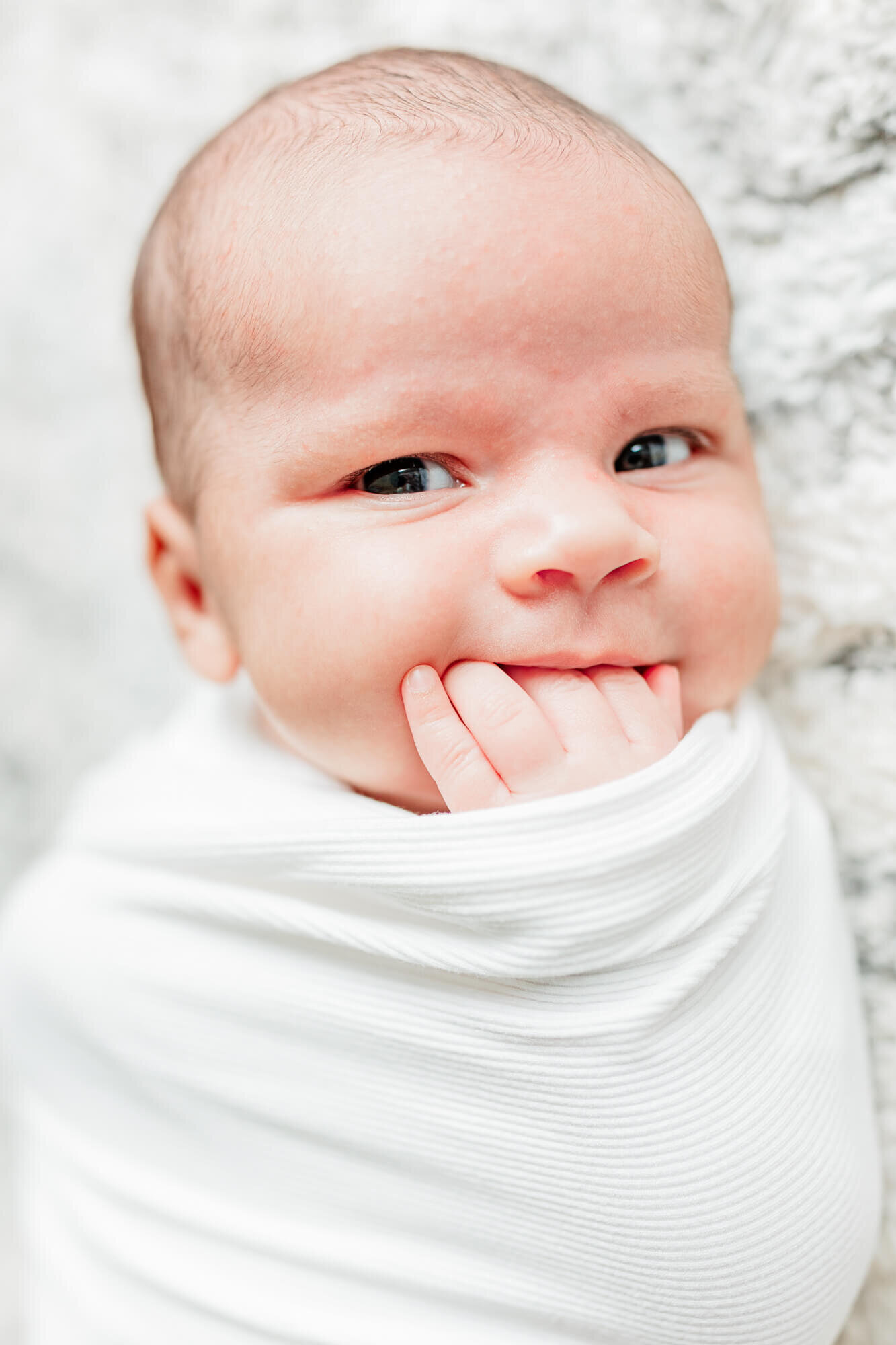 Swaddled alert newborn with hand in her mouth