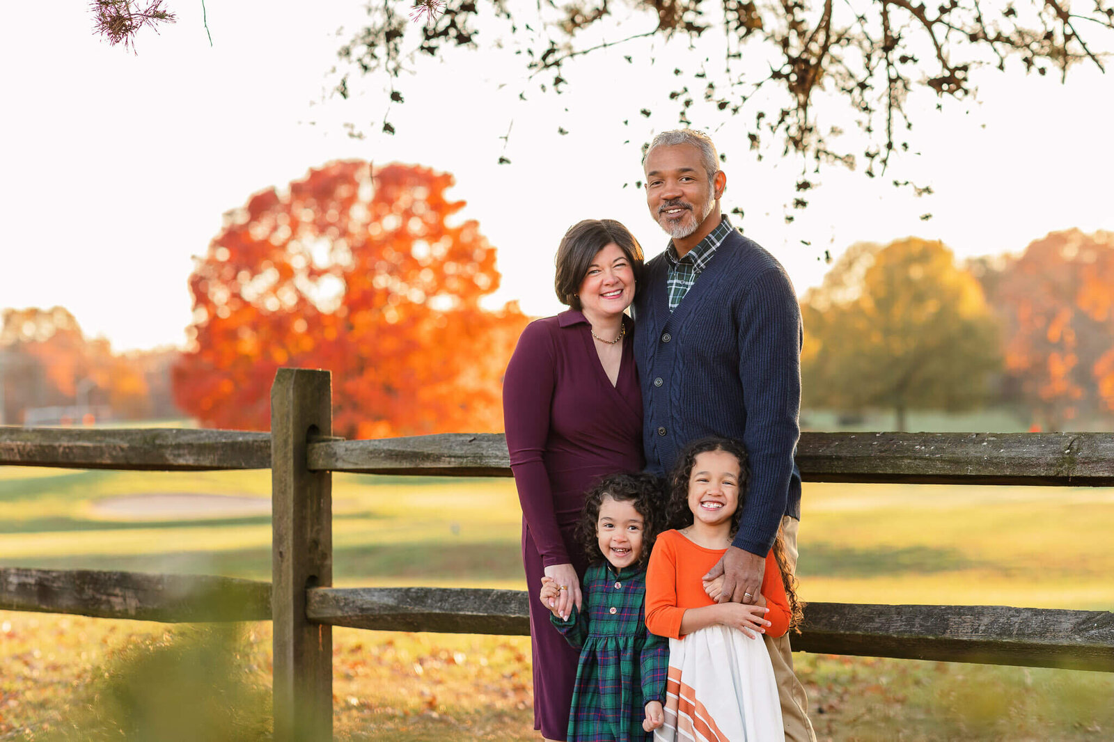 A family of four standing up against a fence