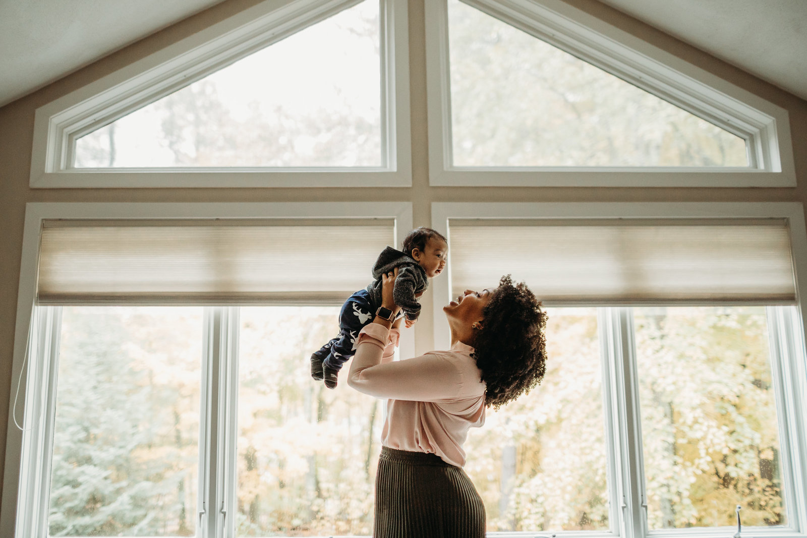 woman holds baby in air by vaulted windows