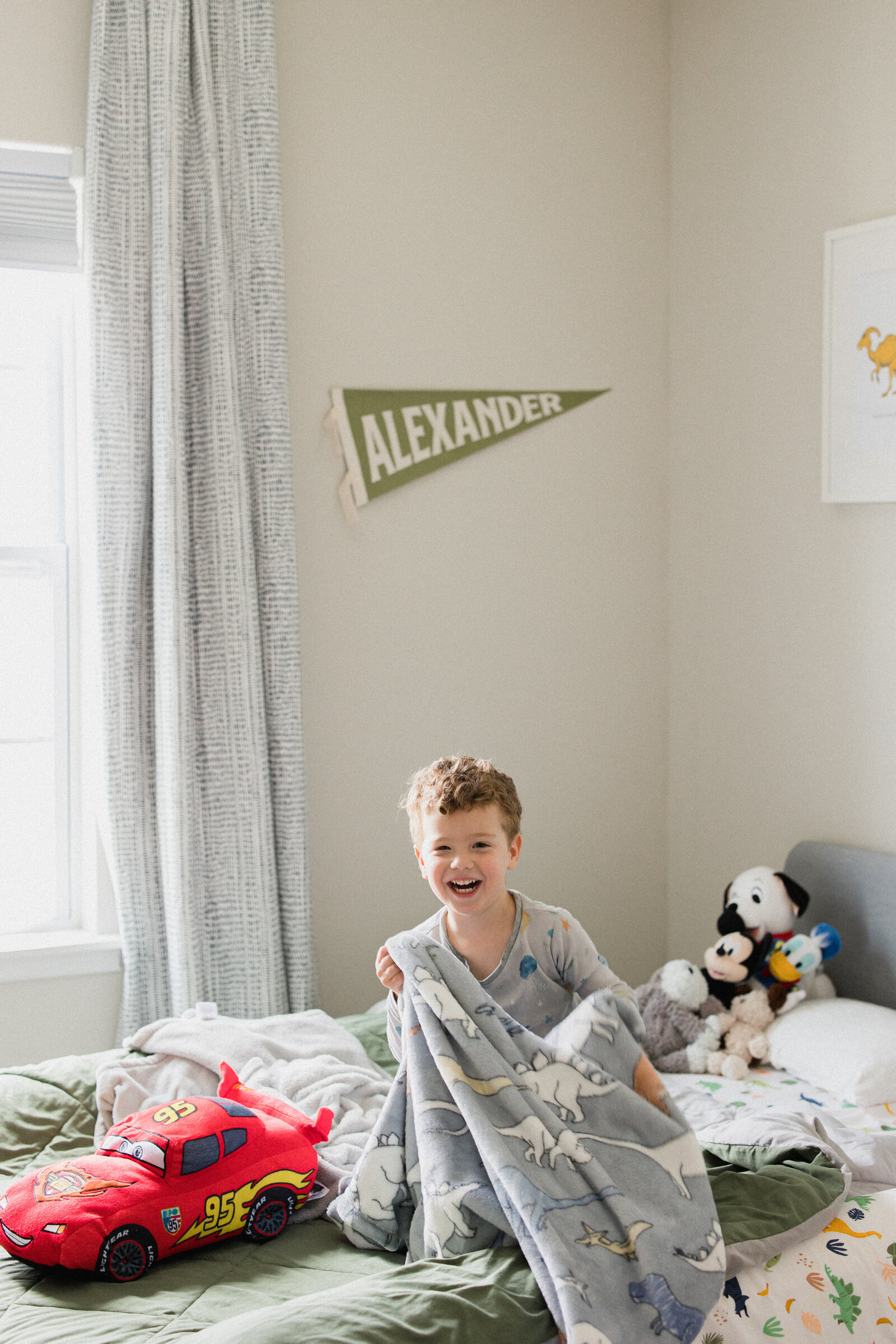 Little boy smiles from bed surrounded by all his stuffed animals