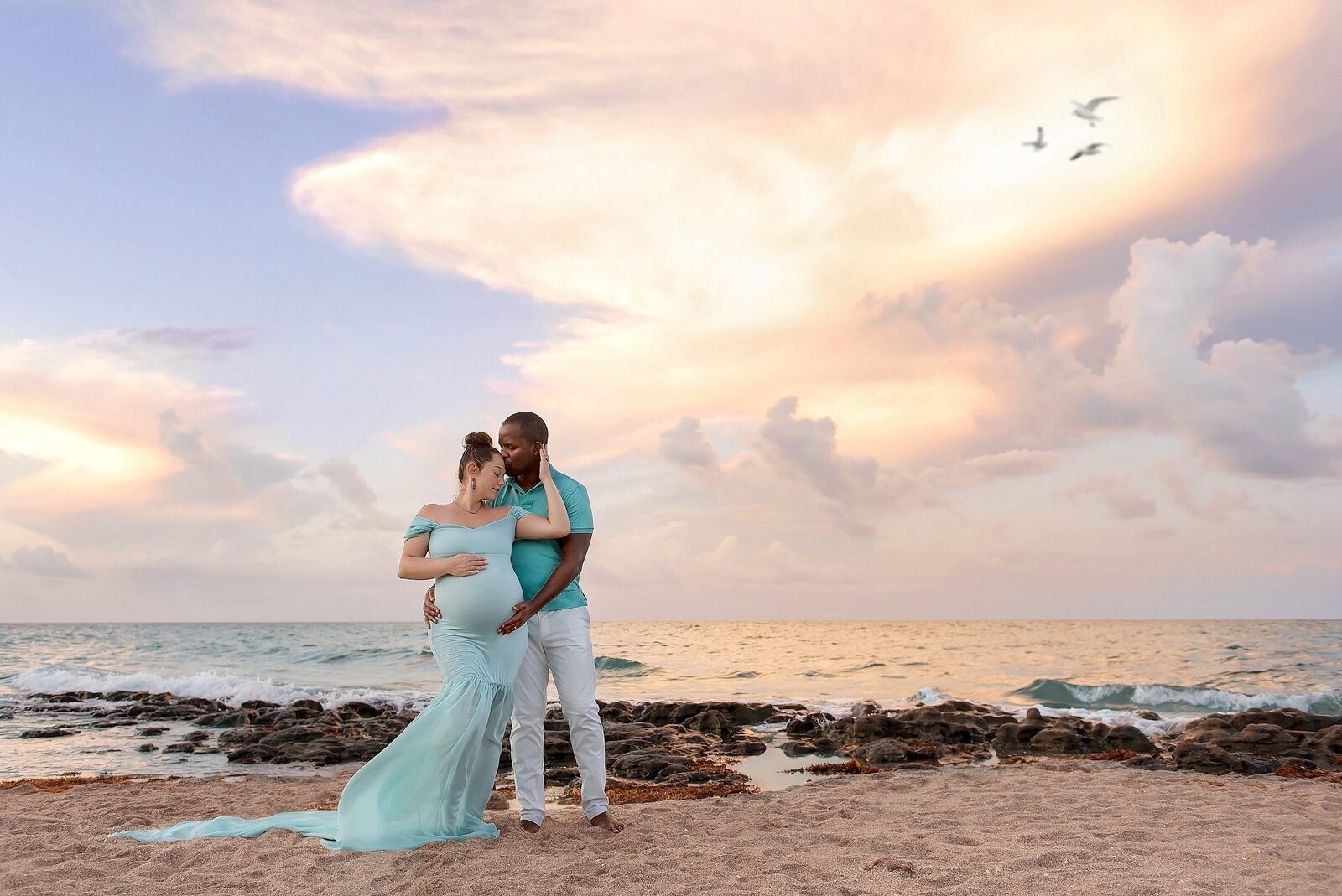 Husband and wife maternity pictures on the beach with rocks in Jupiter, FL.