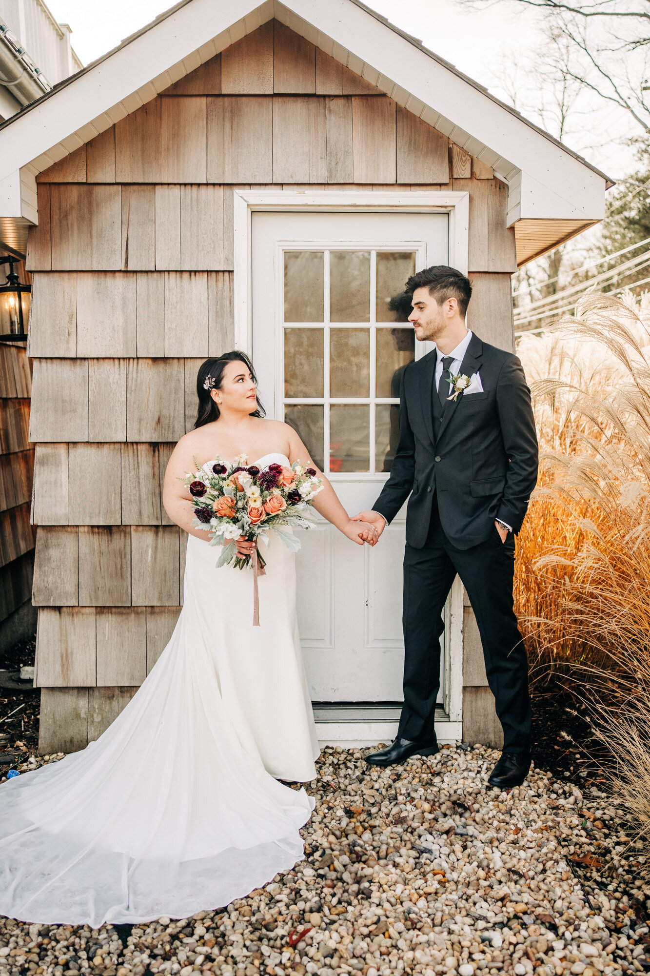 bride and groom holding hands and looking at each other in front of a small wooden shed with a glass door