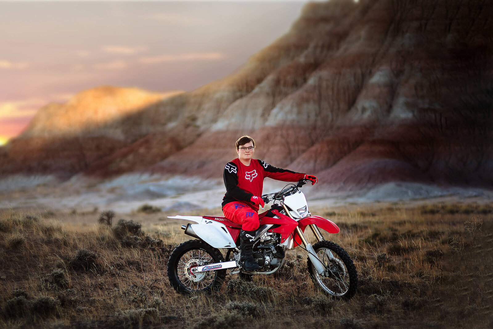 Jackson Hole Senior sitting on his red dirtbike wearing red and black motocross clothing in the desert