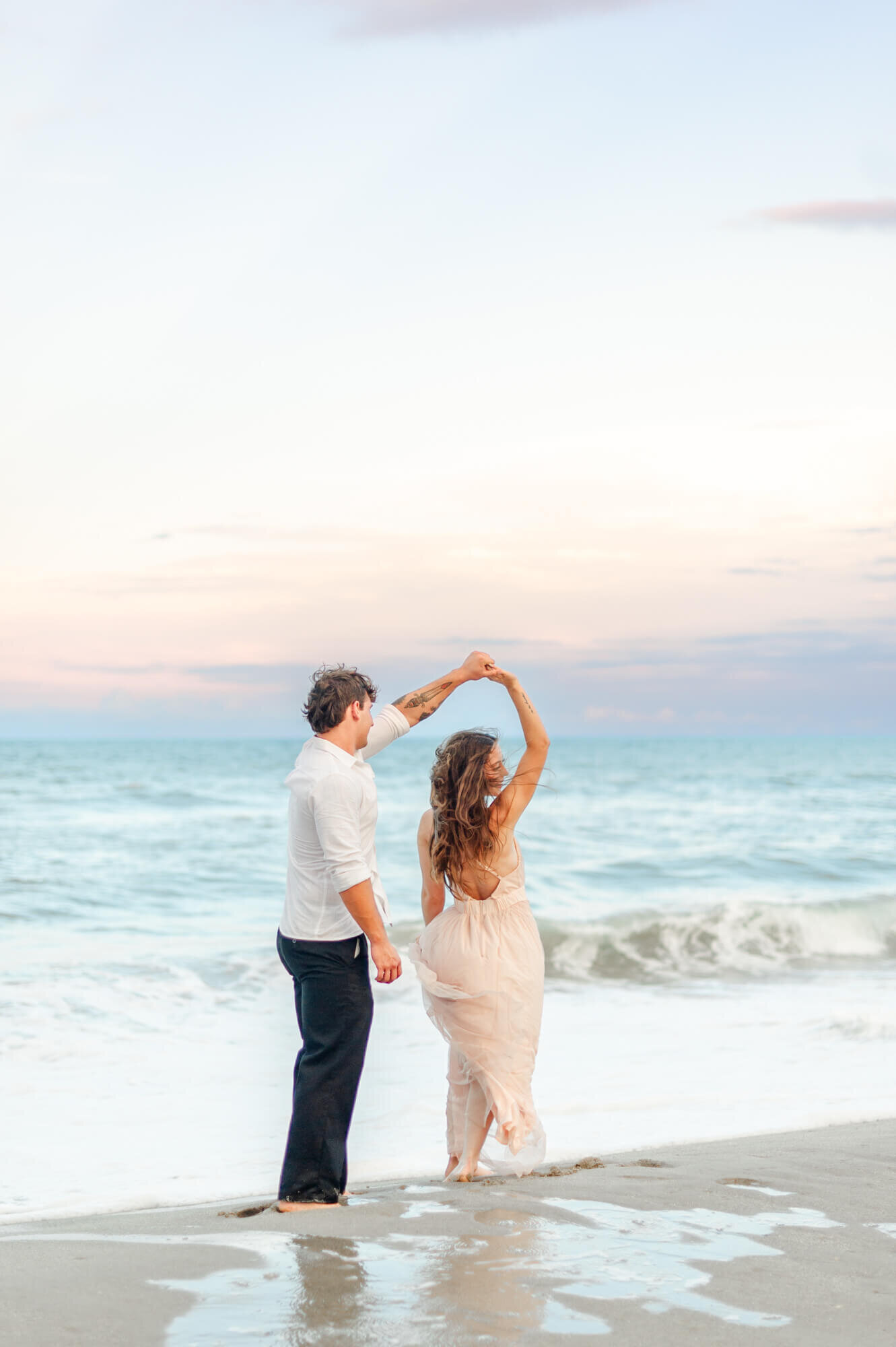 Couple visiting the beach for a picnic dance near the shoreline during their couples photography session