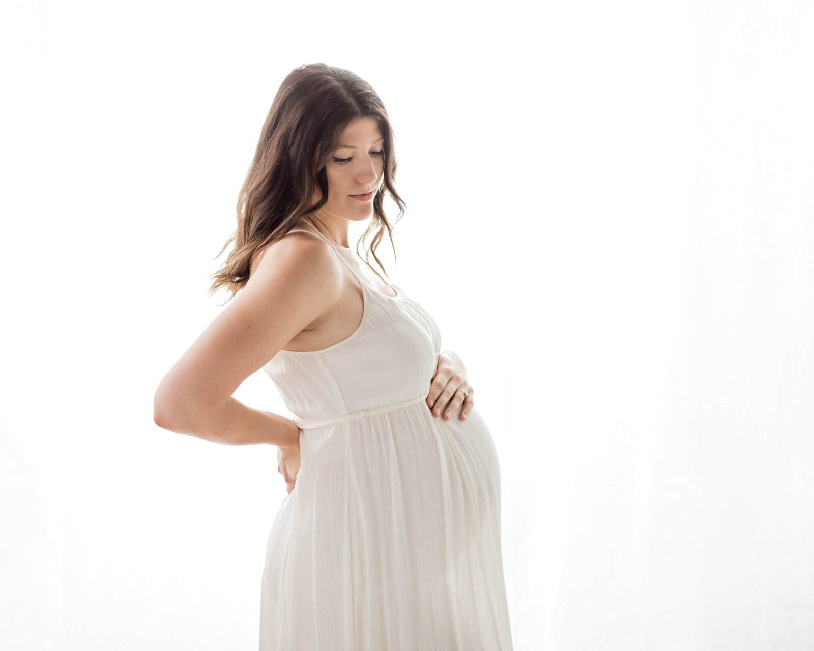 pregnant mother in white maternity dress holding baby bump for maternity photoshoot