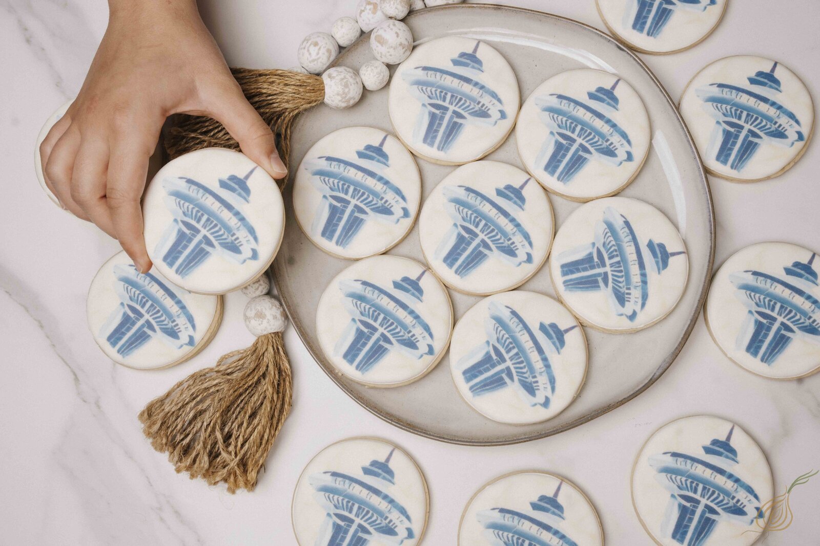 A person holds a tray of cookies, featuring a decorative Space Needle design on the surface.