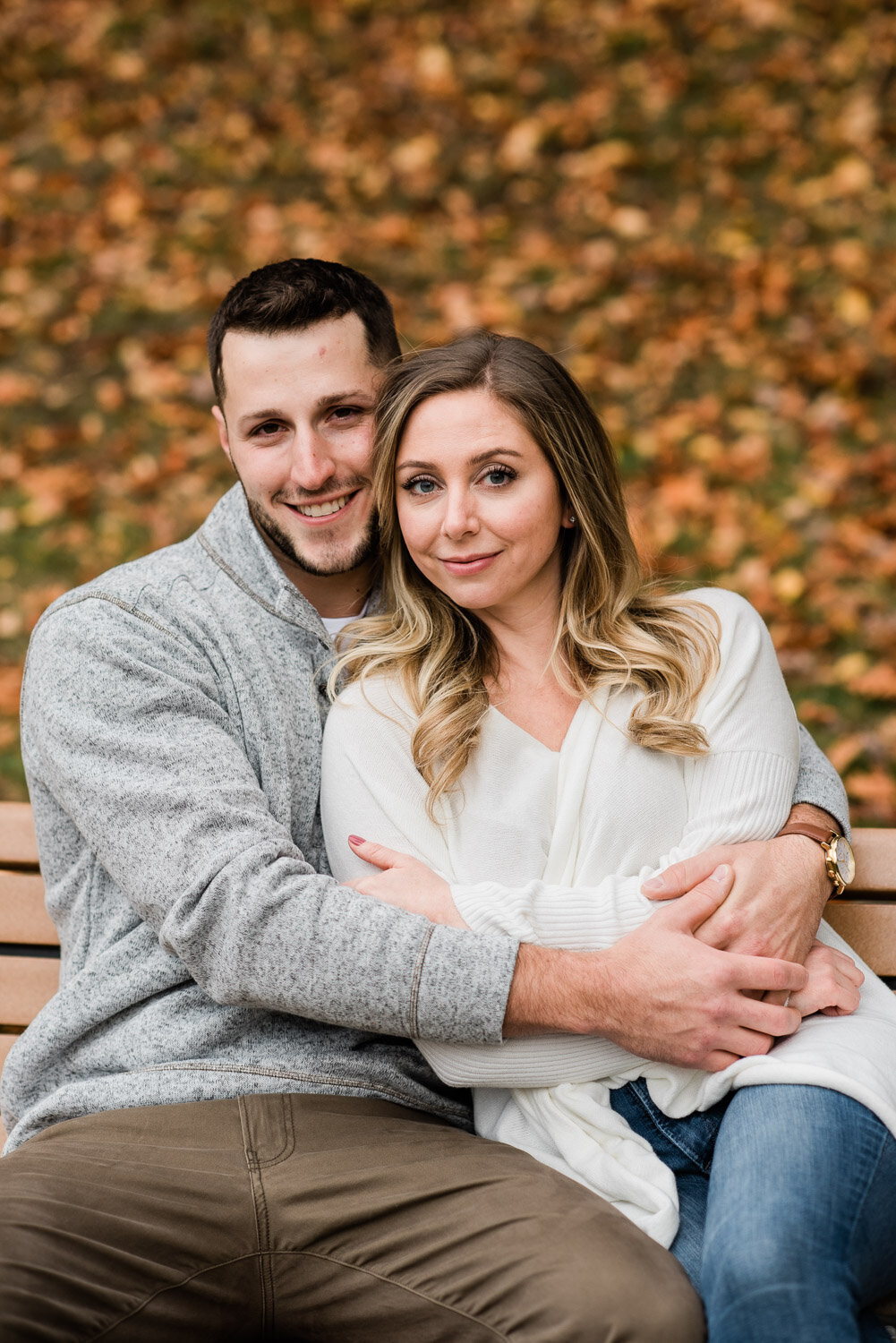 couple sit and snuggle on bench in fall
