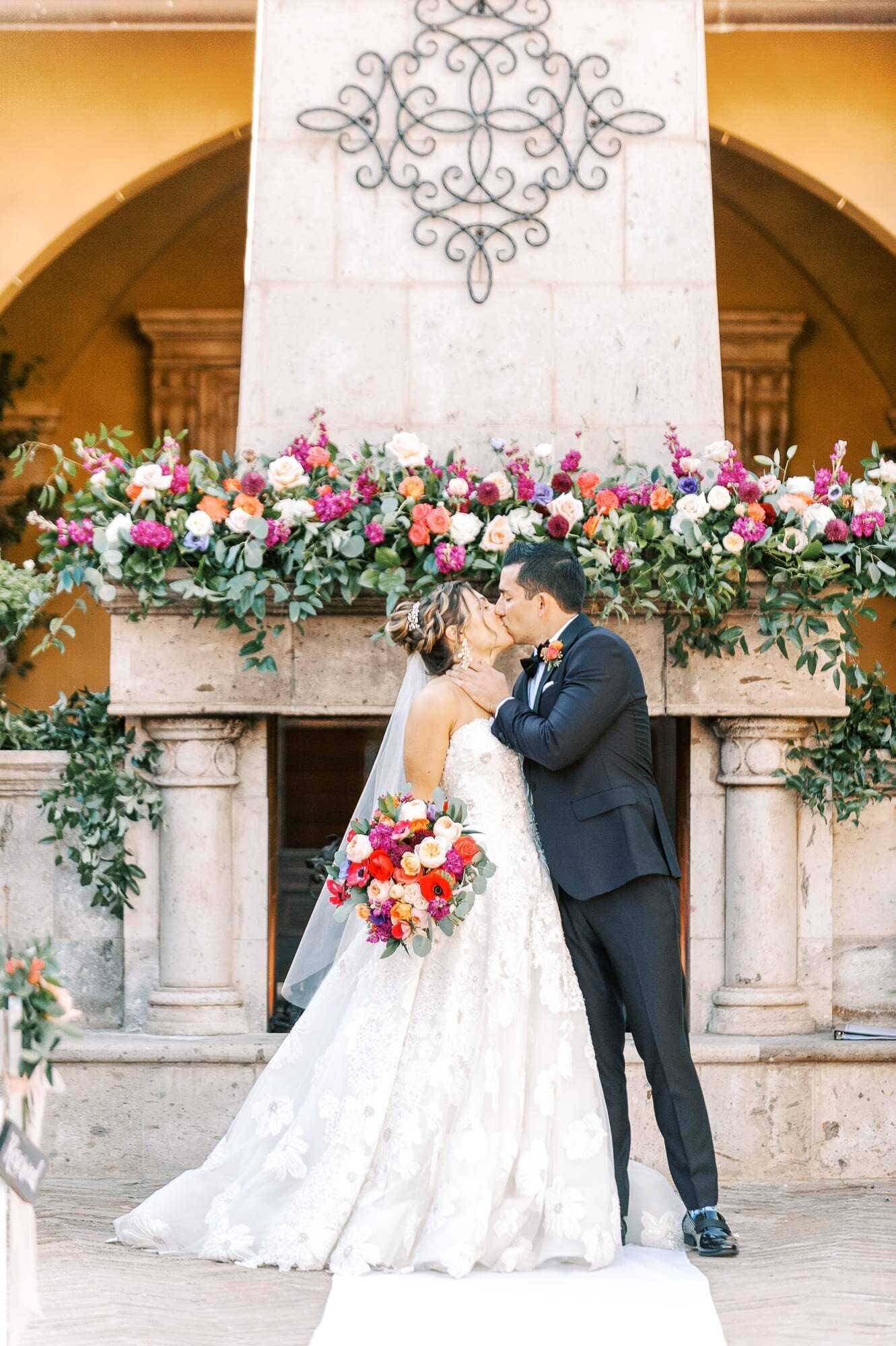 Bride and Groom kissing at Villa Siena with bright spring flowers on the fireplace mantel.