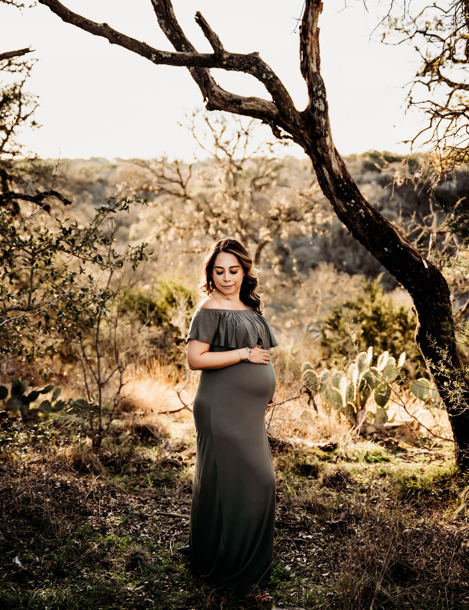 Maternity Photographer, an expectant mother stands in the woods wearing a dress