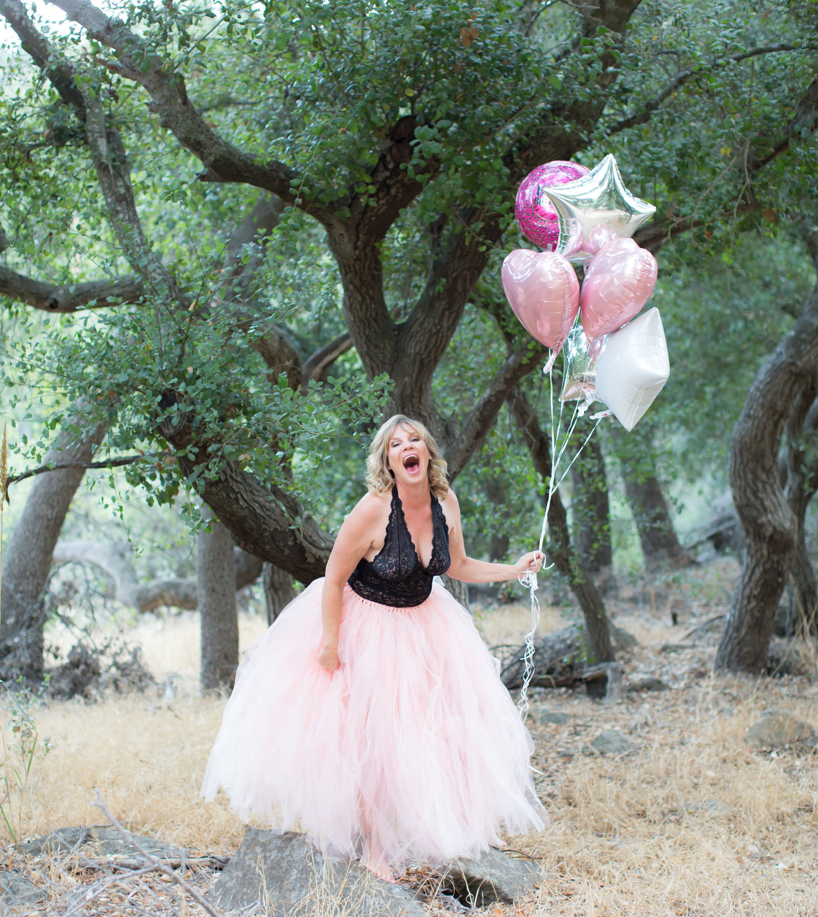 Woman holding pink balloons outside in pink skirt and black top