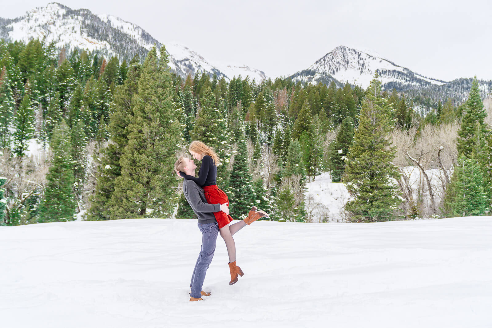 utah engagement photography of a man standing in the snow lifting up his fiancee at Tibble Fork Reservoir, American Fork