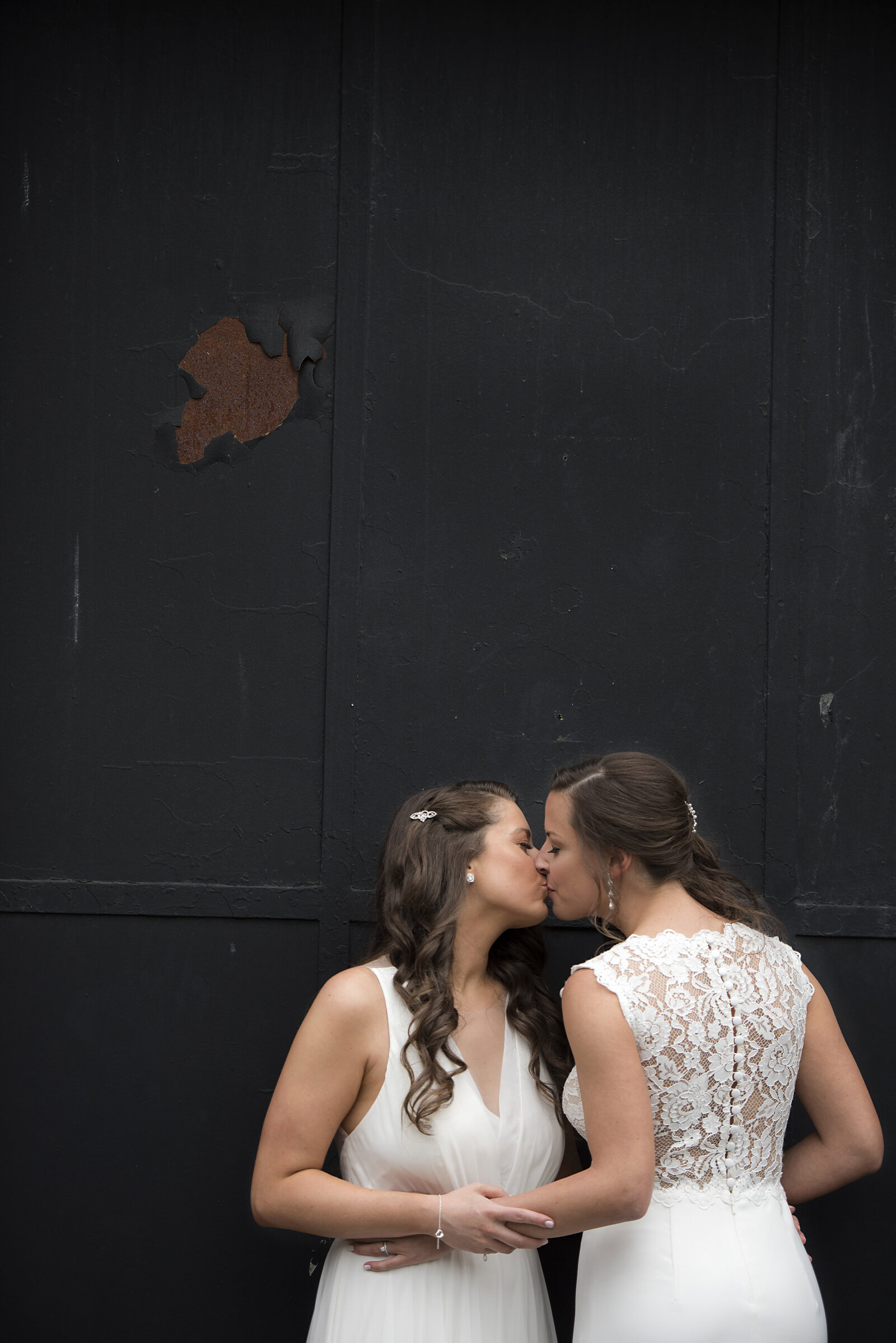 A newlywed couple kissing as they each face a different direction 