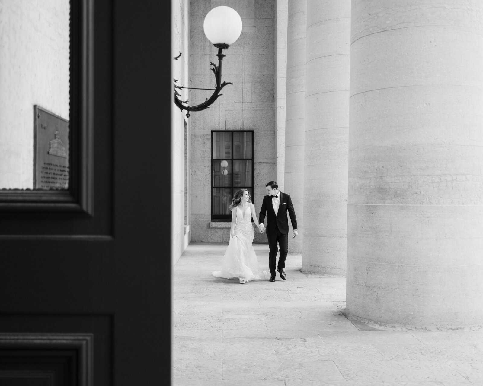 Bride and groom hold hands and jog on the portico of the Ohio Statehouse