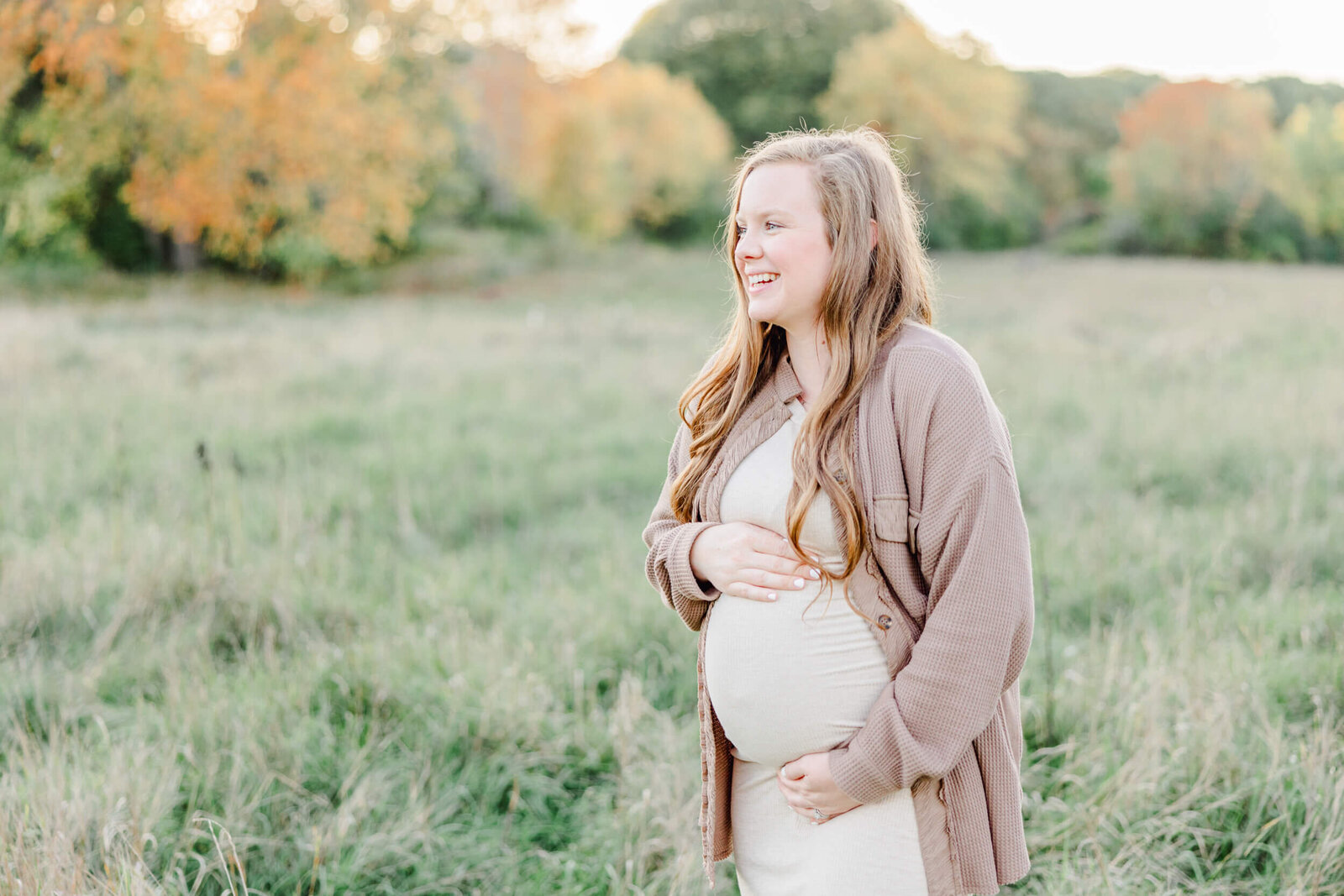 Pregnant woman in a meadow looks up and smiles