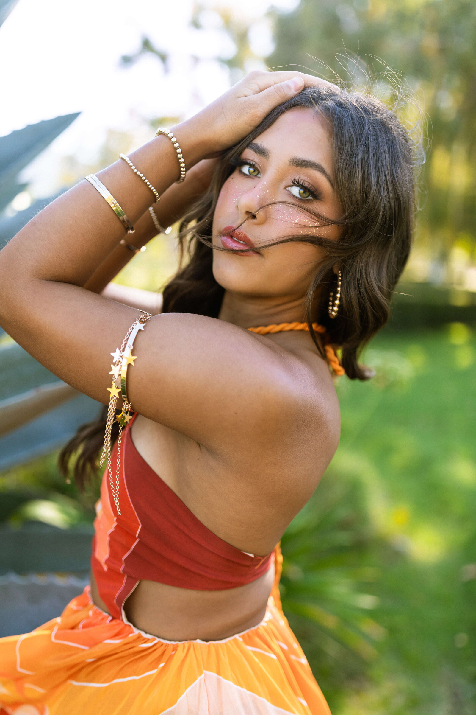 girl with dark hair wearing colorful outfit and lots of gold jewelry posing for a picture in a garden