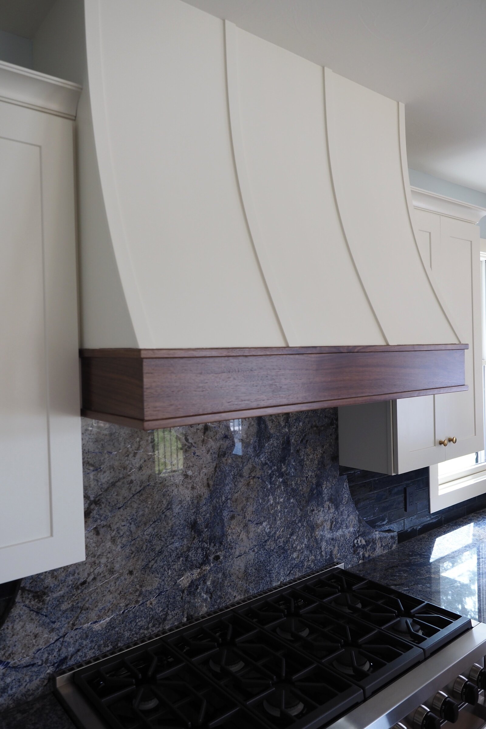 Custom range hood with swooping front and wood trims.
