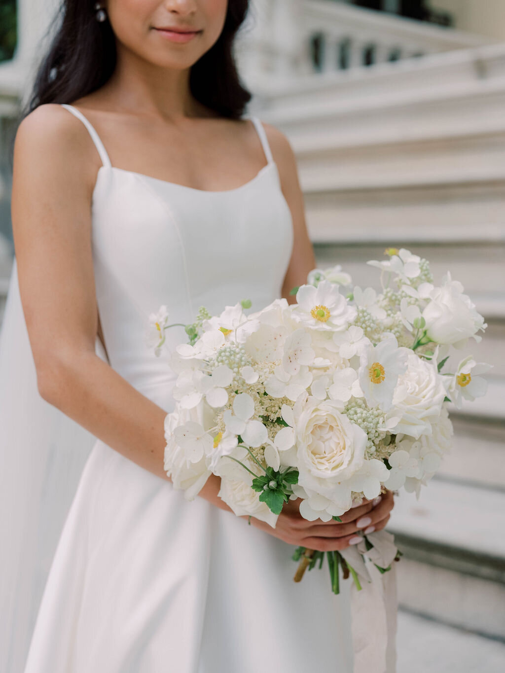 Bride holding bridal bouquet with white garden roses, white Japanese anemone, and white quick-fire hydrangea.